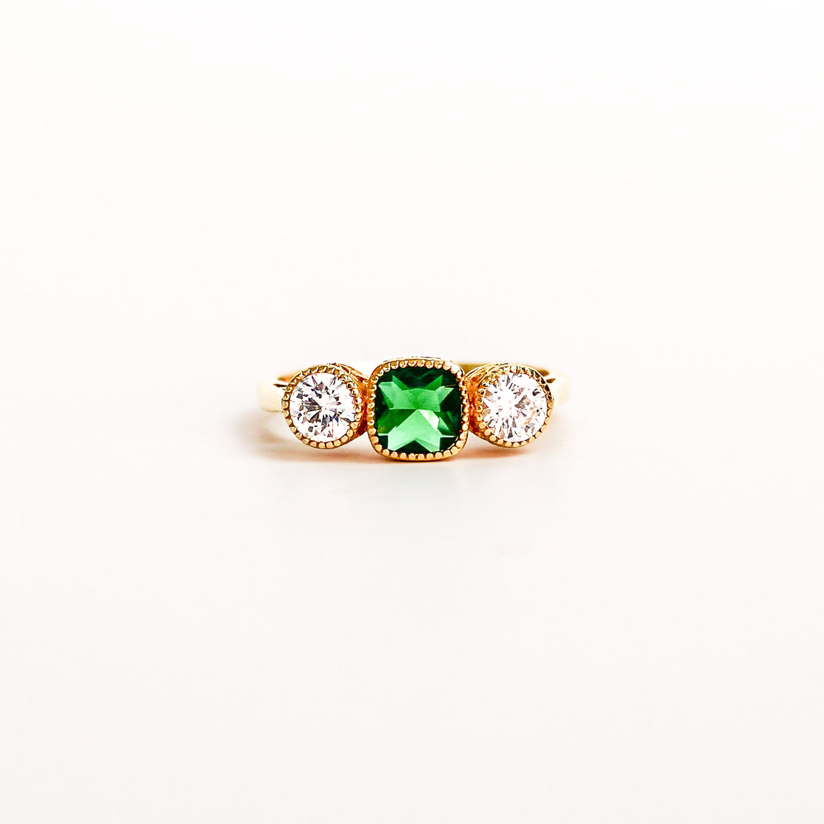 Three Stone Edwardian Ring on white background, square center emerald gemstone, two white side gemstones, ether jewelry