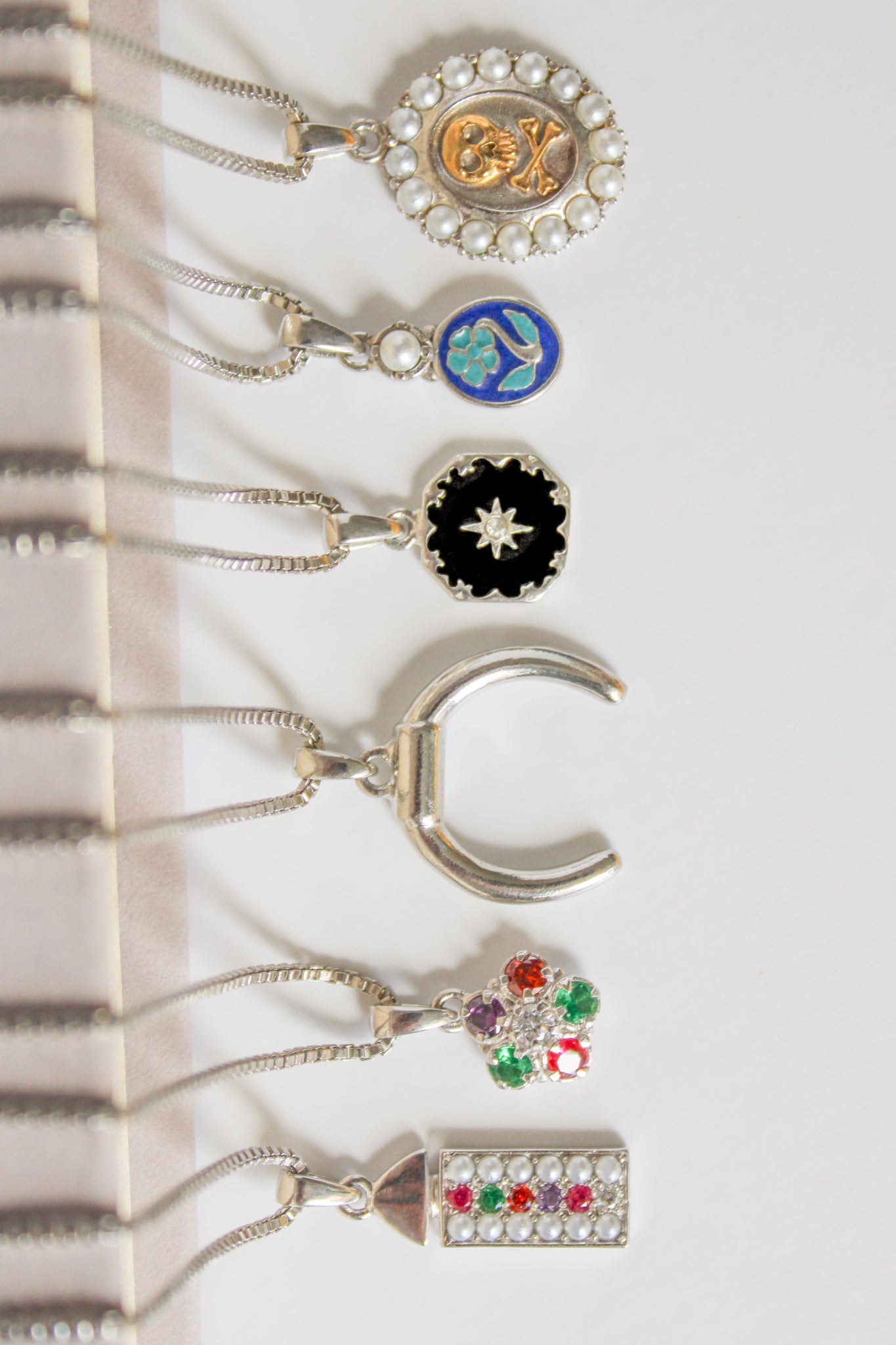 Regent sterling silver necklace draped over book with full Regard pendant collection, pearl-paved acrostic rectangular pendant, Ether Jewelry