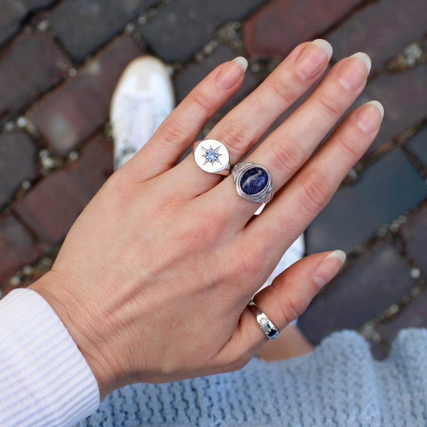 Hand wearing multiple signet rings and victorian roma ring with blue stones on a blurred brick background, Ether Jewelry