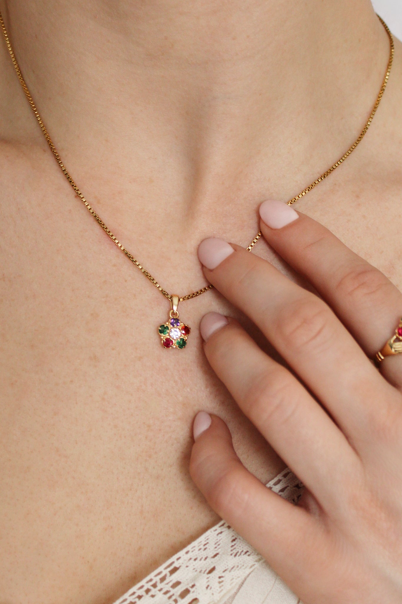Regard Bloom Necklace in 18k gold vermeil on model touching pendant, acrostic REGARD floral cluster necklace, Ether Jewelry