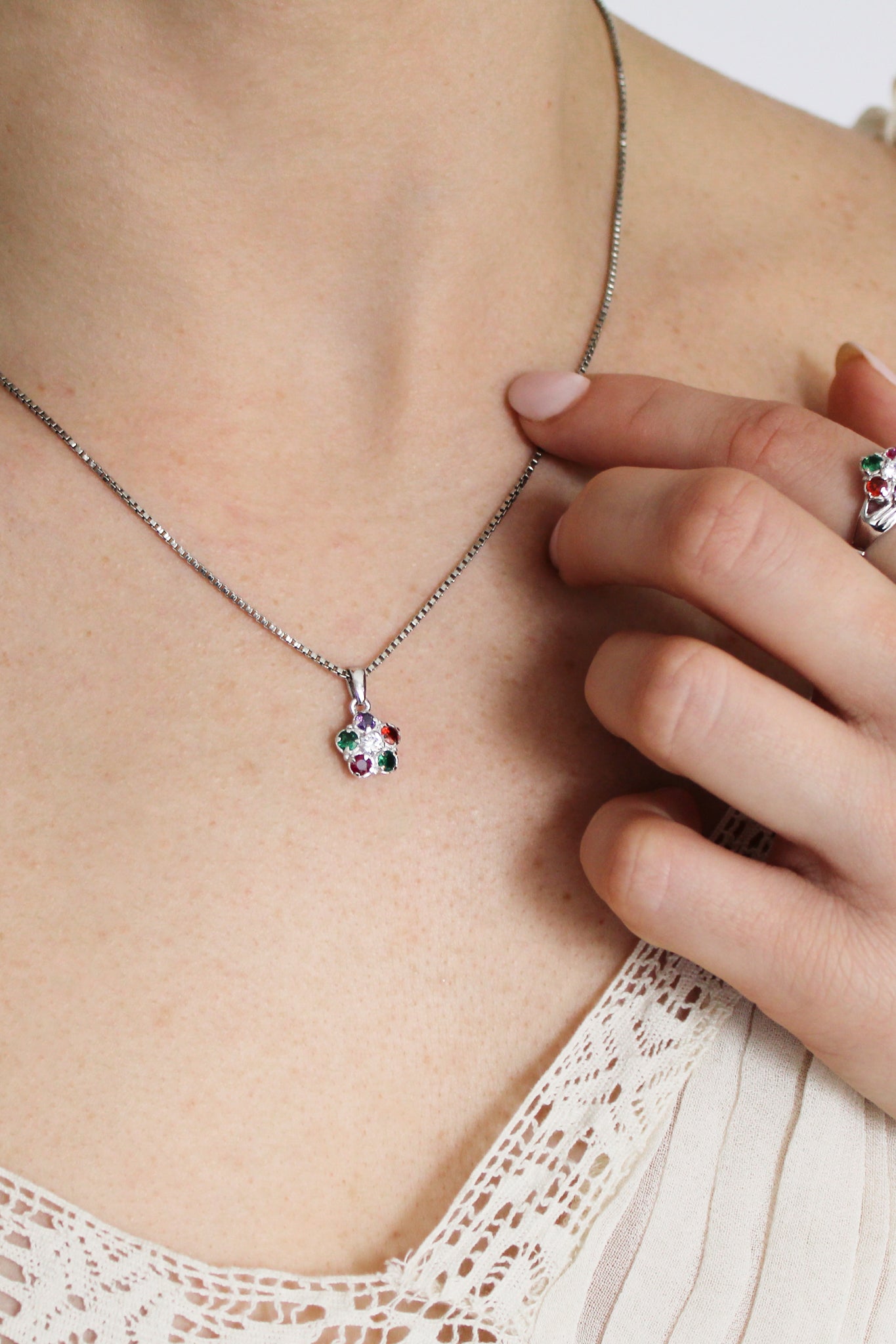 Regard Bloom Necklace in sterling silver on model touching pendant, acrostic REGARD floral cluster necklace, Ether Jewelry