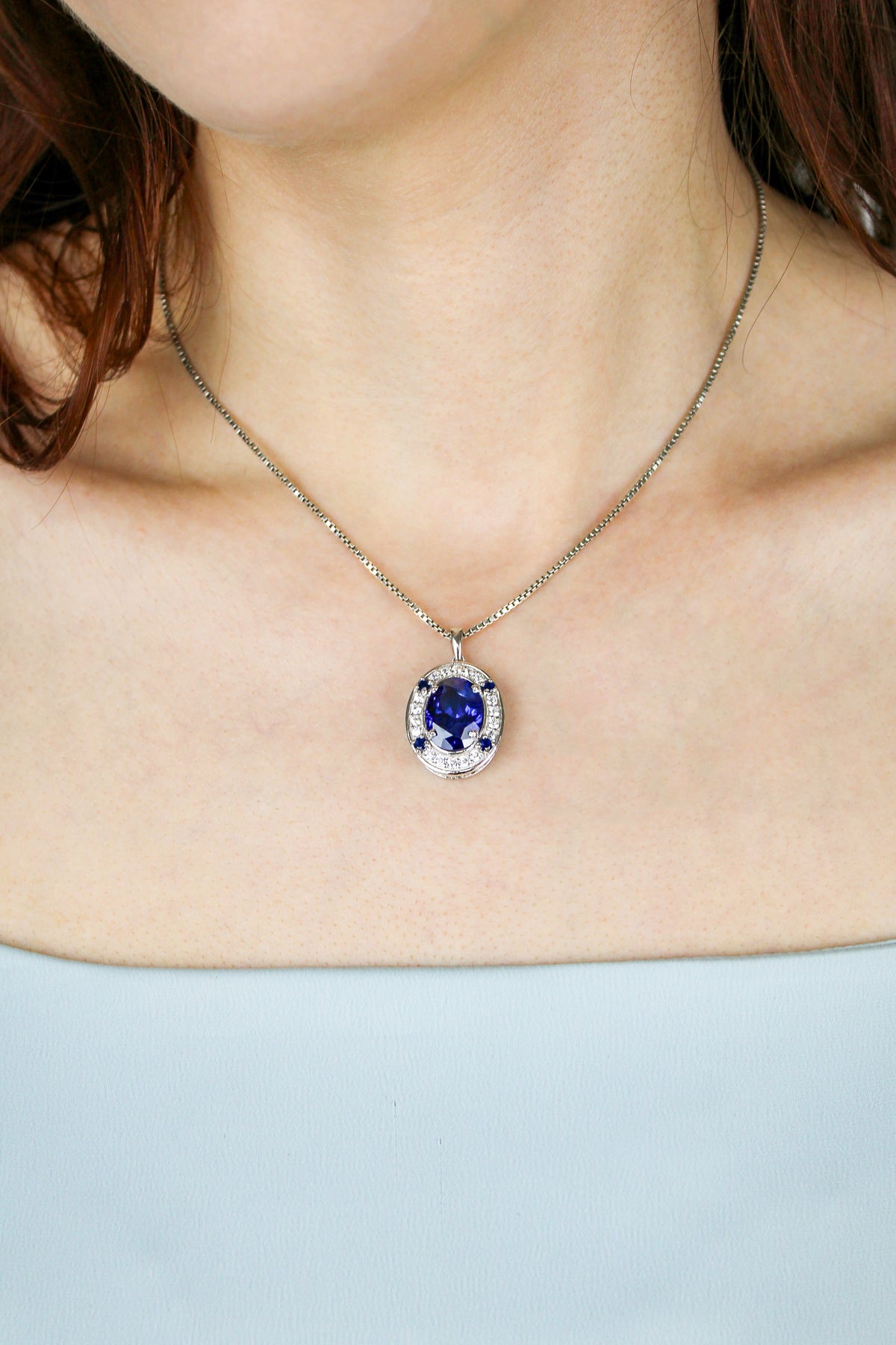 Detailed close-up of model wearing silver Heartline Necklace, luminous sapphire gemstone reflecting quiet strength, Ether Jewelry