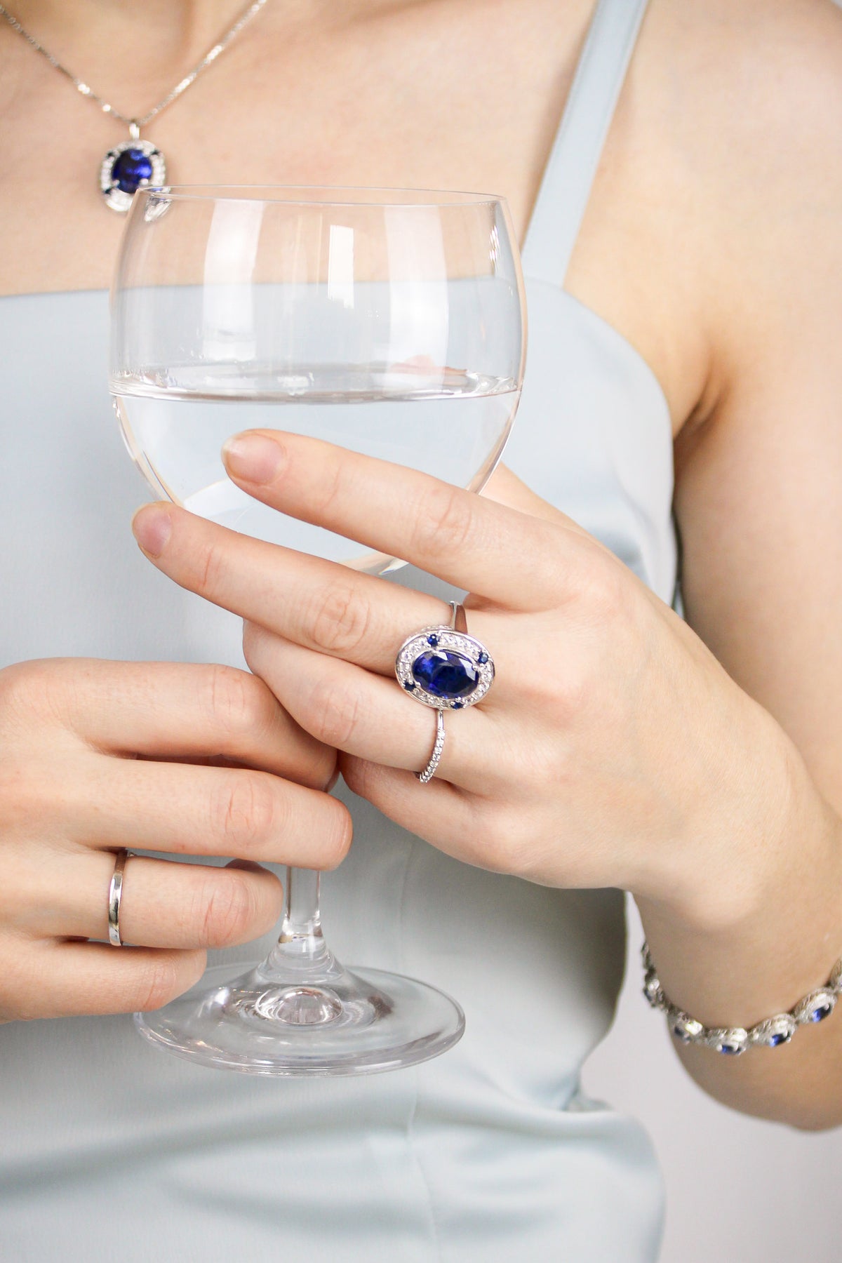 Close-up of silver Legacy Collection, Ring, Bracelet, Neckalce on model’s hand holding wine glass, reflecting refined craftsmanship and ethereal light, Ether Jewelry