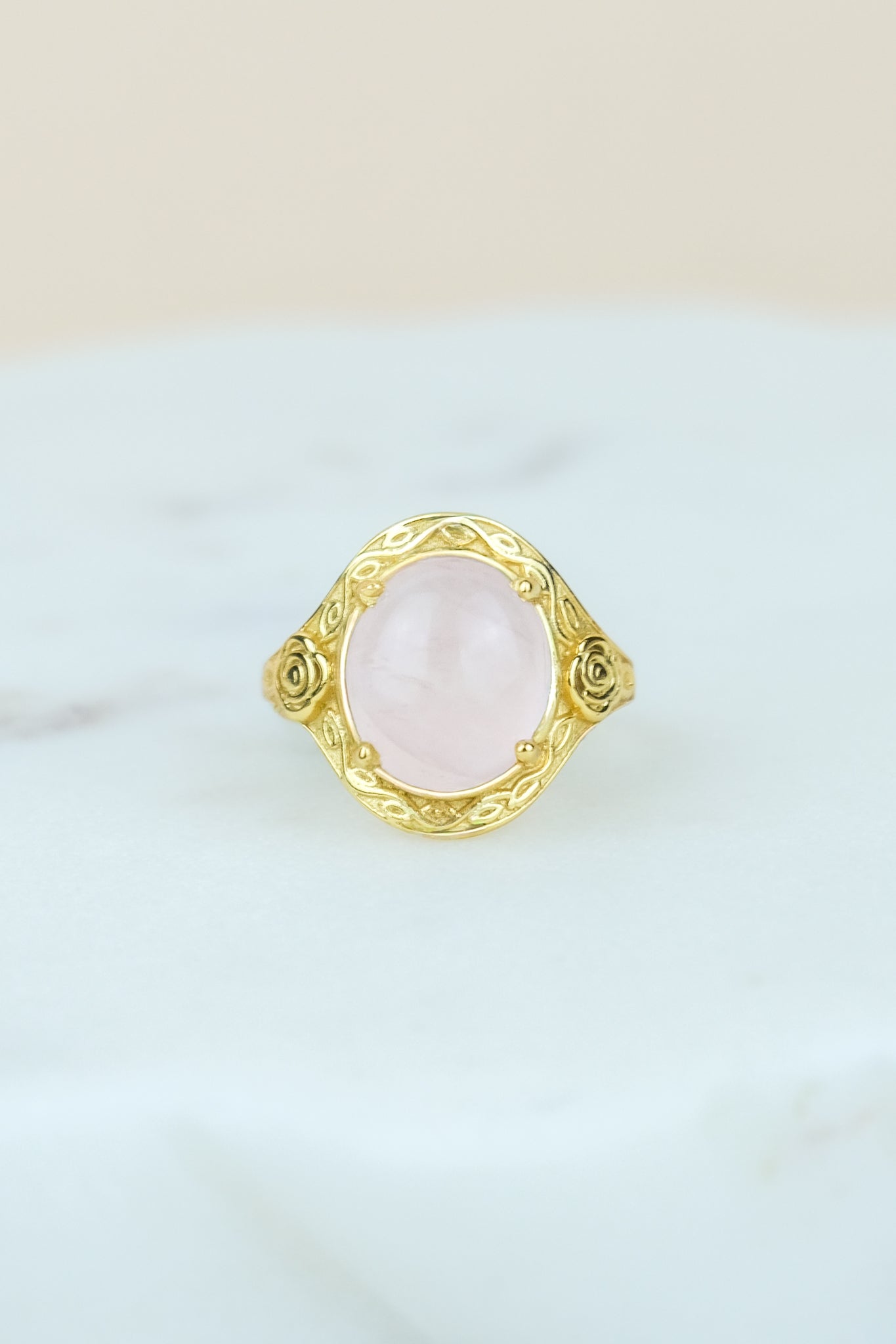 Gold romantic heir signet Ring with pink quartz gemstone and flower engravings on a white marble background