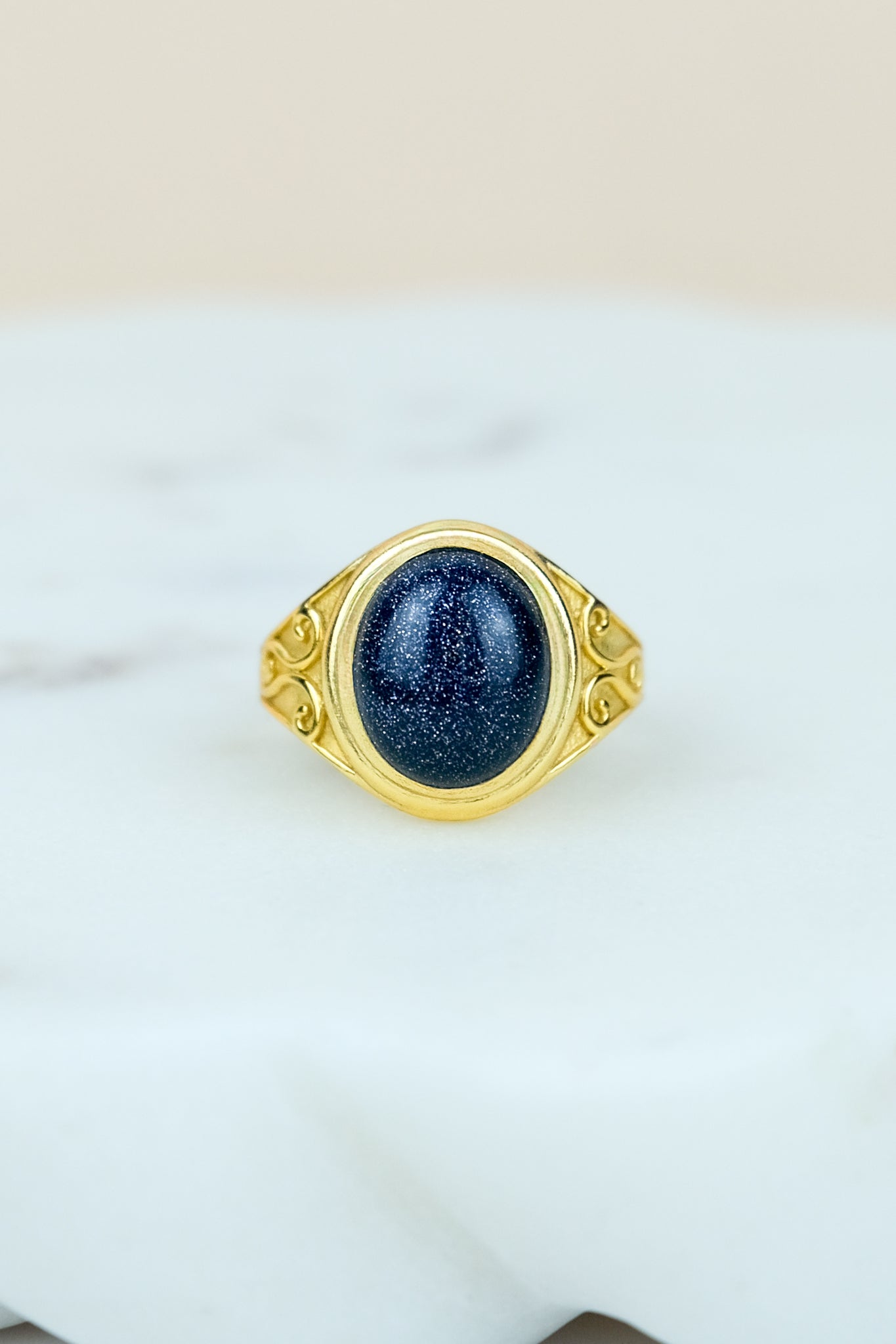 Gold night keeper signet ring with a blue sandstone on a marble background