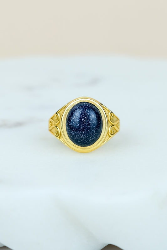 Gold night keeper signet ring with a blue sandstone on a marble background