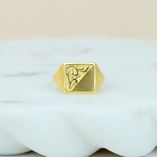 Gold square architect ring with a geometric design on a white marble background