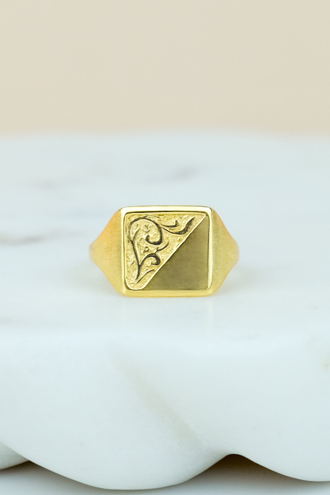 Gold square architect ring with a geometric design on a white marble background