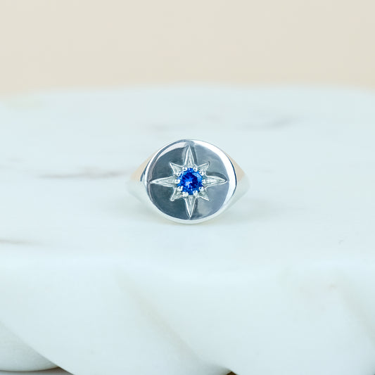 Sterling Silver Wayfinder signet ring with a blue gemstone on a marble background