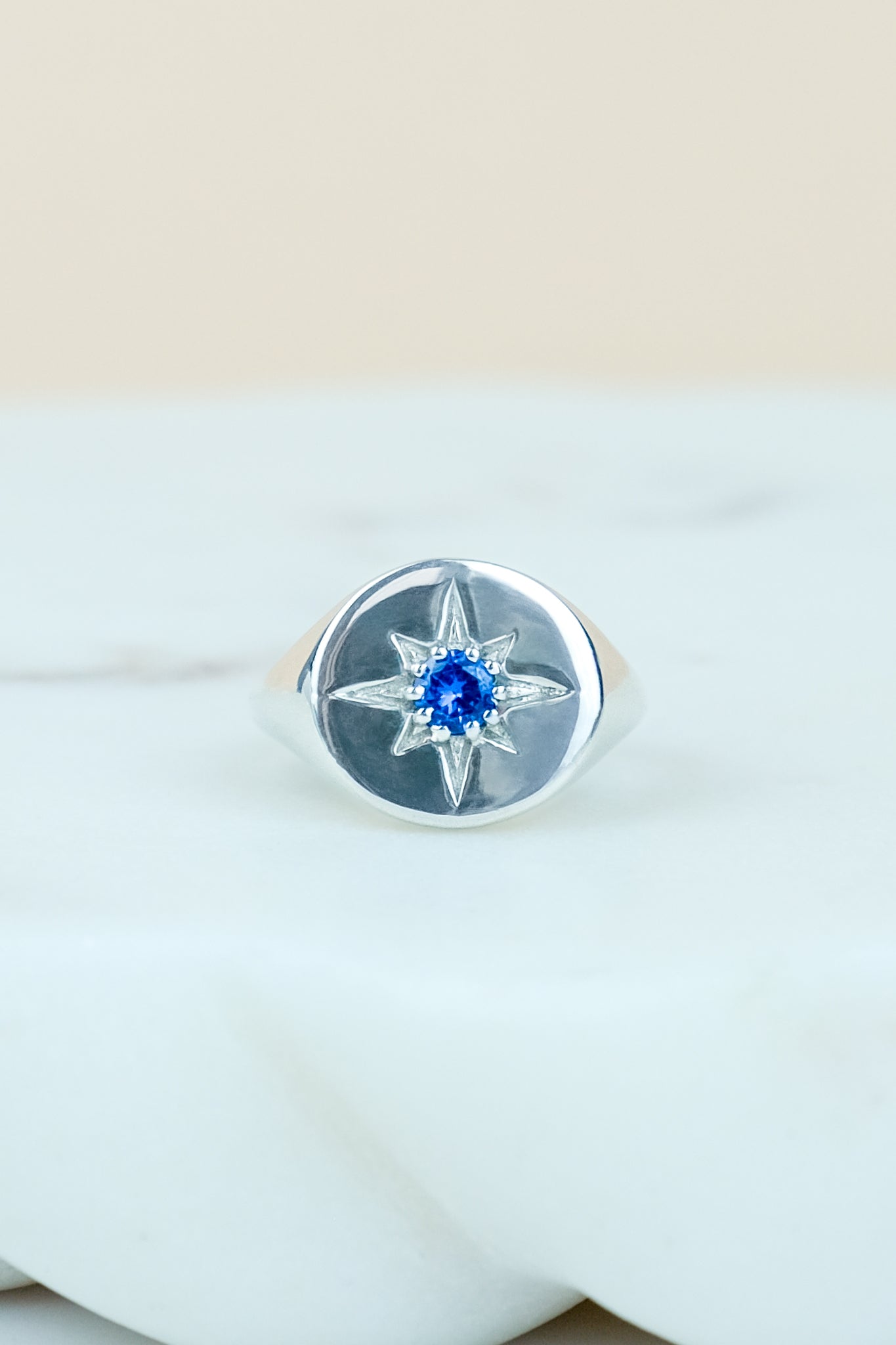 Sterling Silver Wayfinder signet ring with a blue gemstone on a marble background