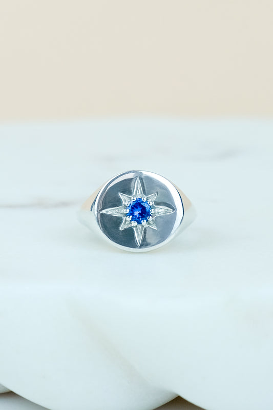 Sterling Silver Wayfinder signet ring with a blue gemstone on a marble background