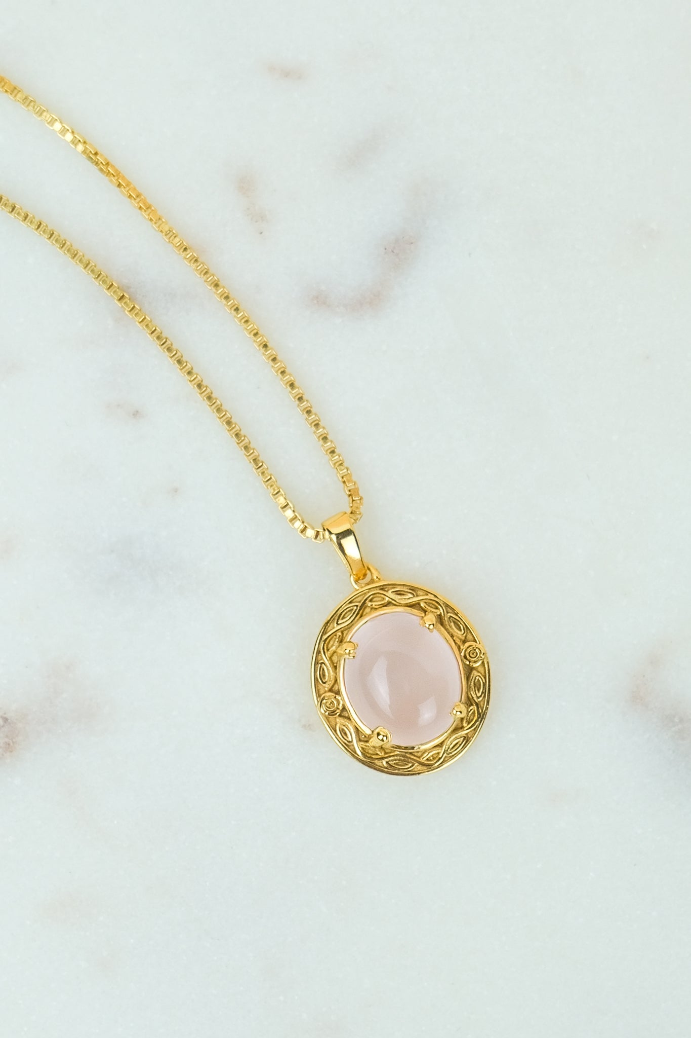 Gold Romantic Heir necklace with a pink quartz stone pendant on a marble surface