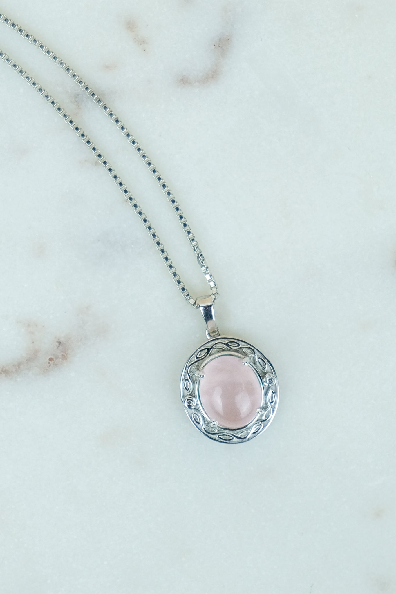Romantic Heir Necklace with a pink quirtz stone pendant on a marble background