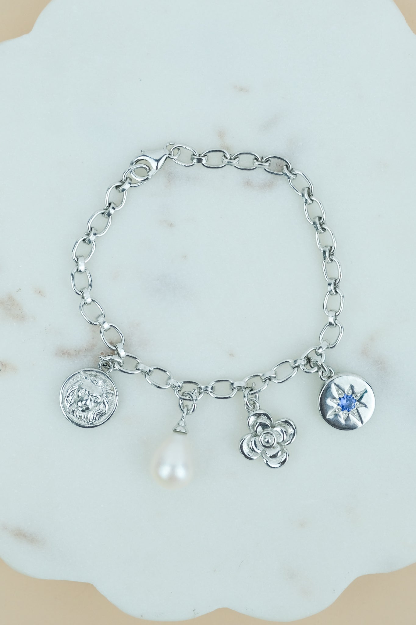 the archivist bracelet Silver bracelet rhodium plated with various charms on a light blue scalloped background