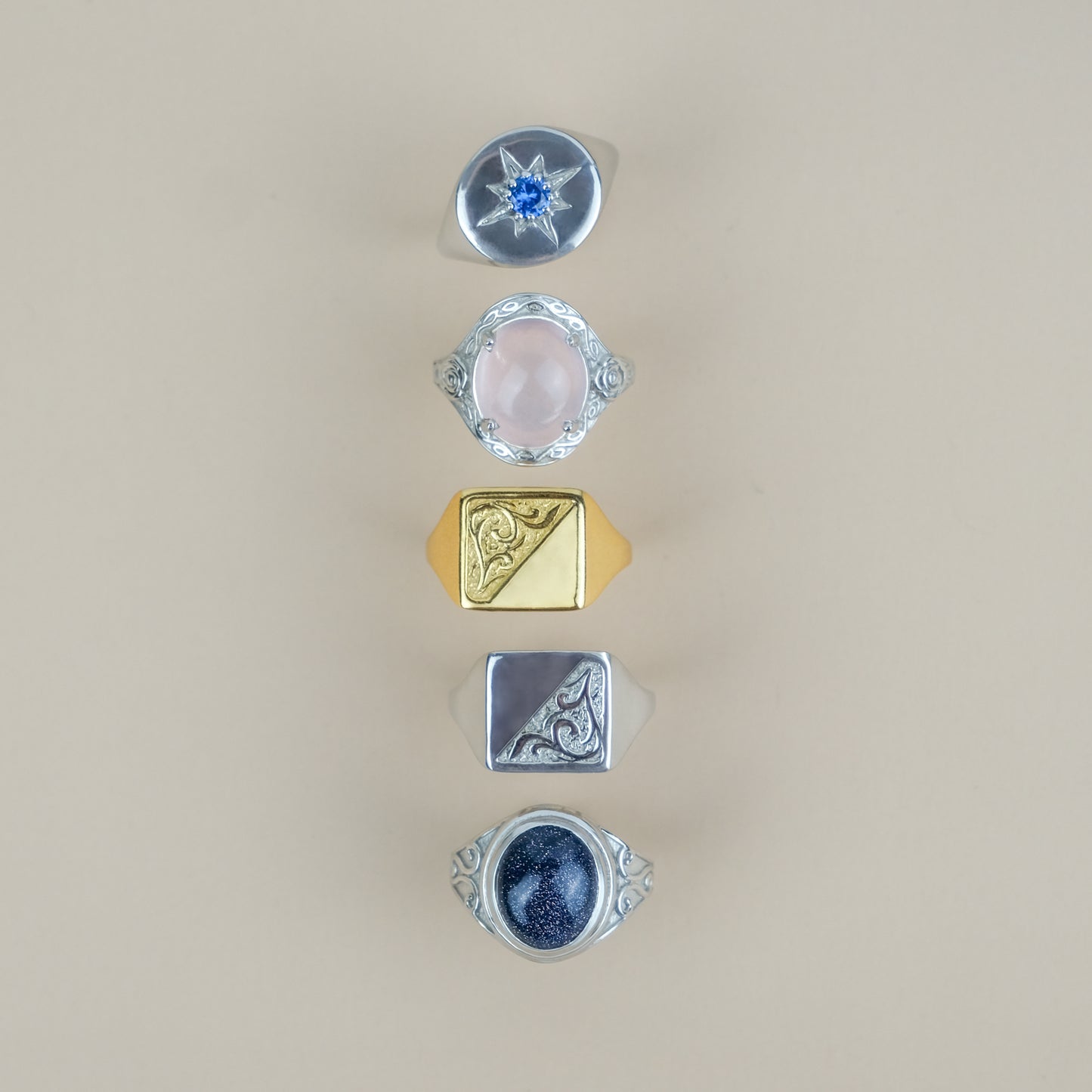 Five different sterling silver signet rings with various designs and gemstones on a beige background