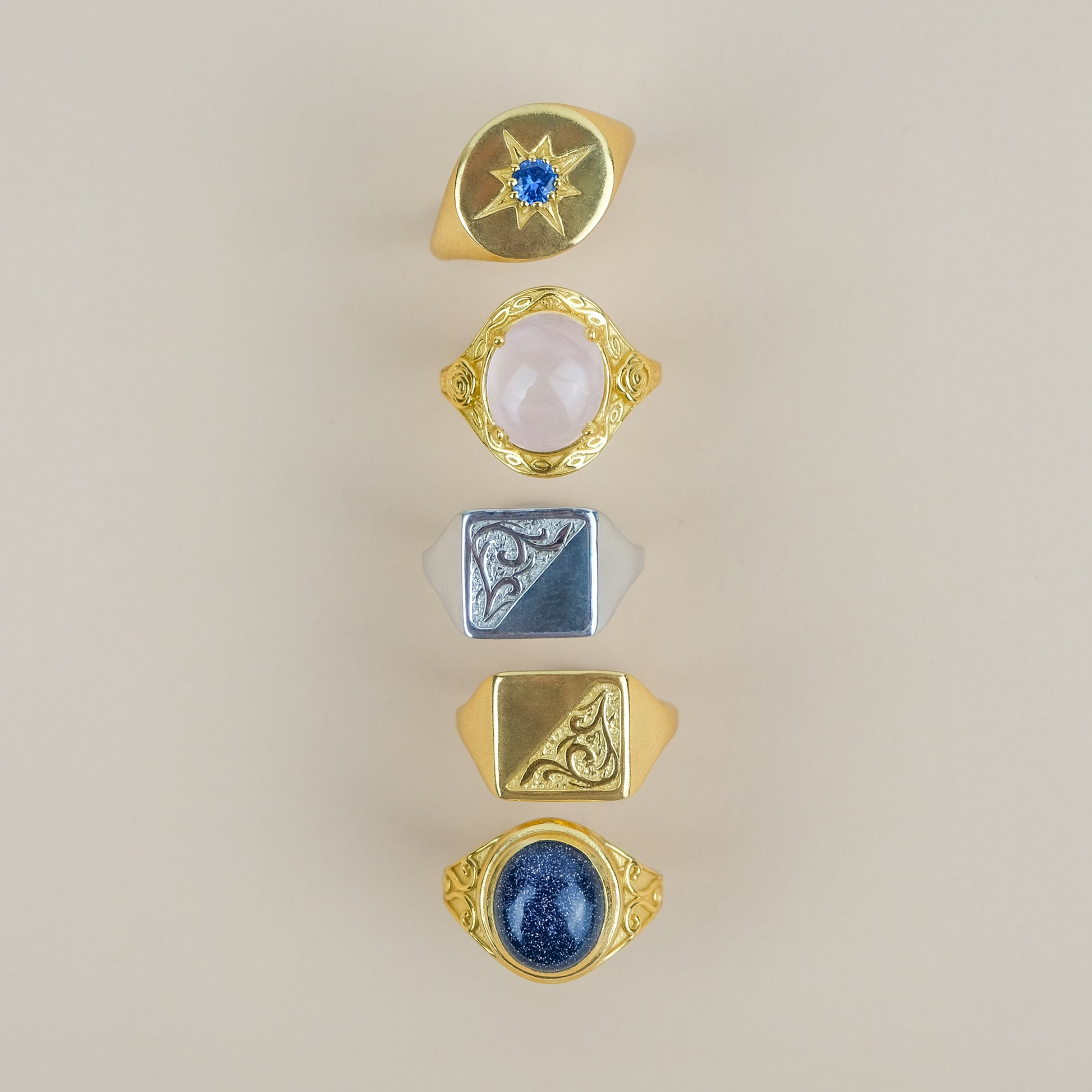 Five gold signet rings with various gemstones on a beige background
