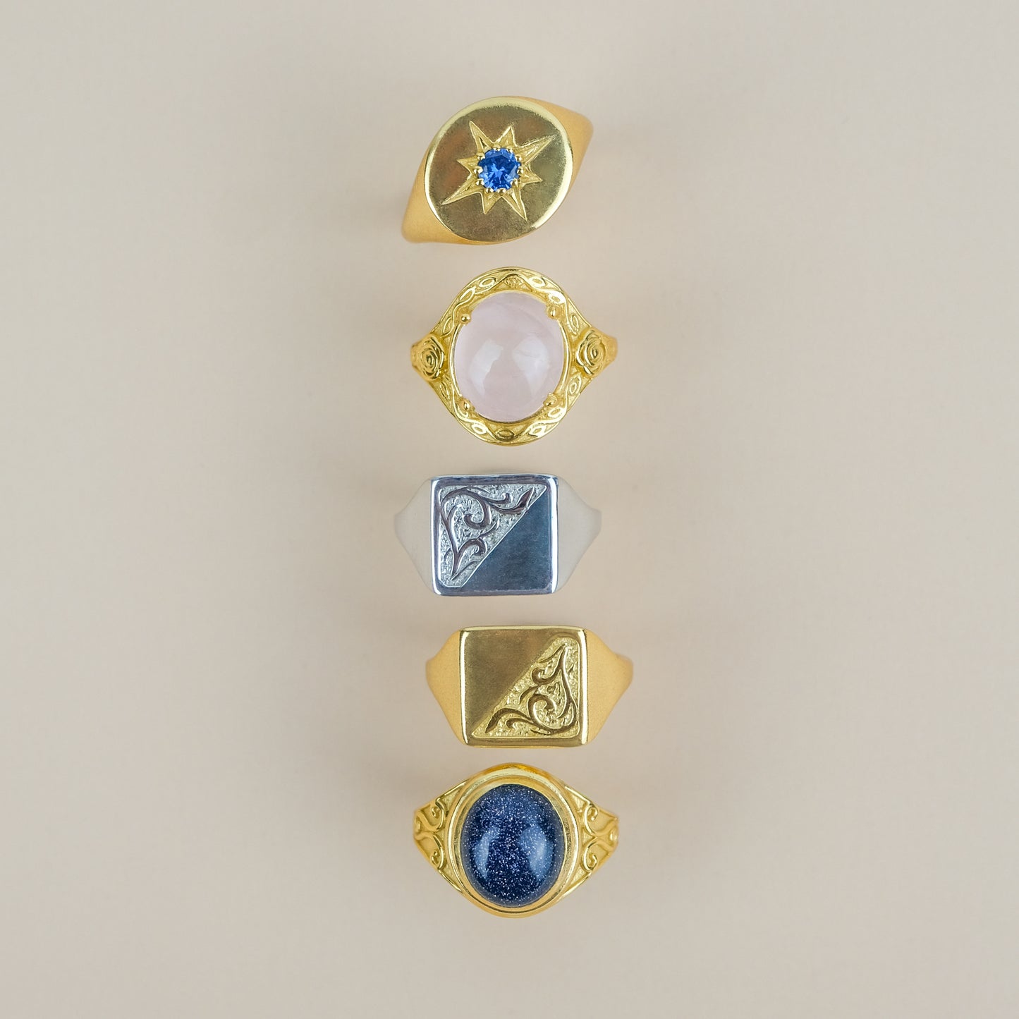 Five gold signet rings with various gemstones on a beige background