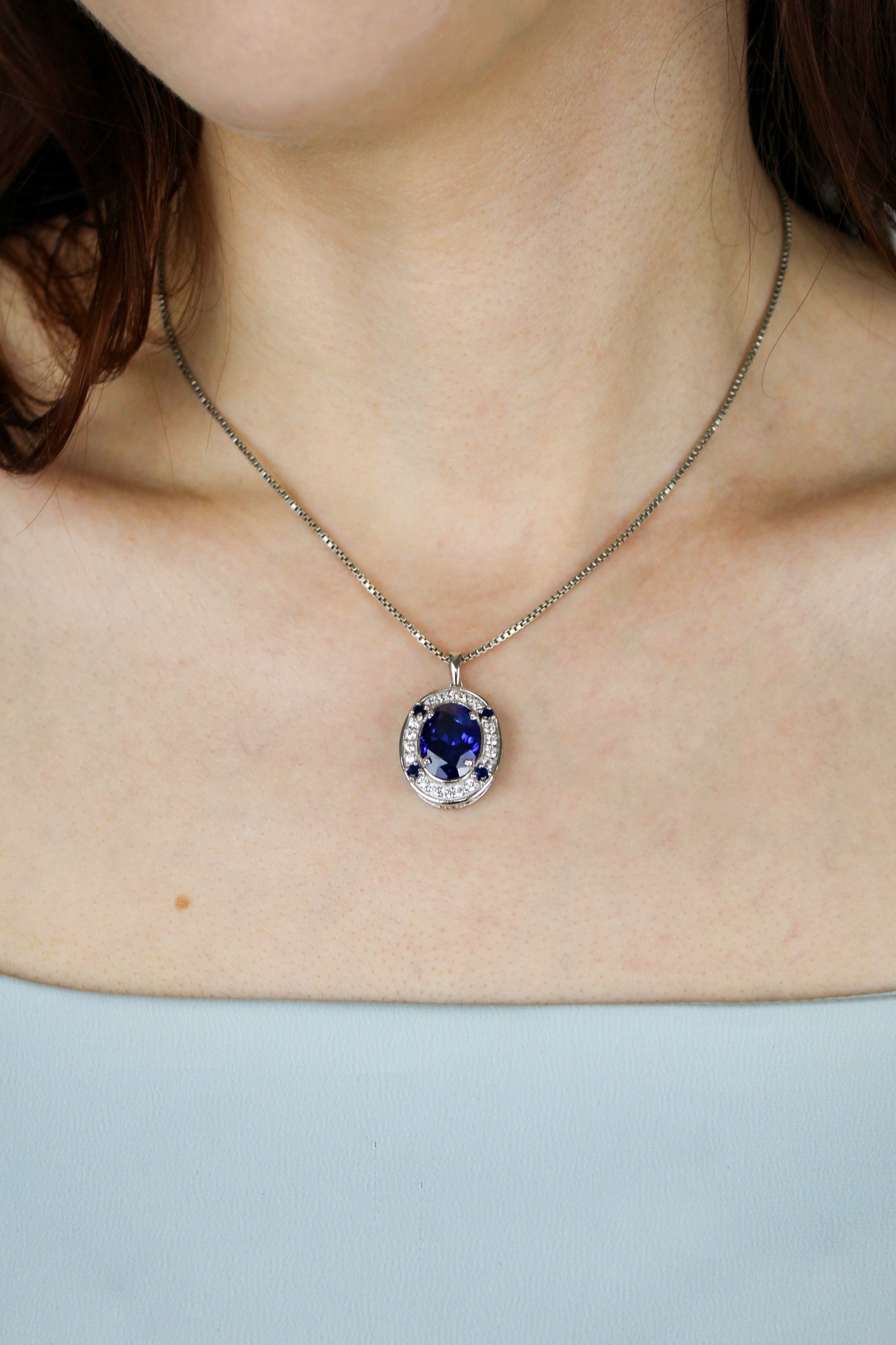 Detailed close-up of model wearing silver Heartline Necklace, luminous sapphire gemstone reflecting quiet strength.