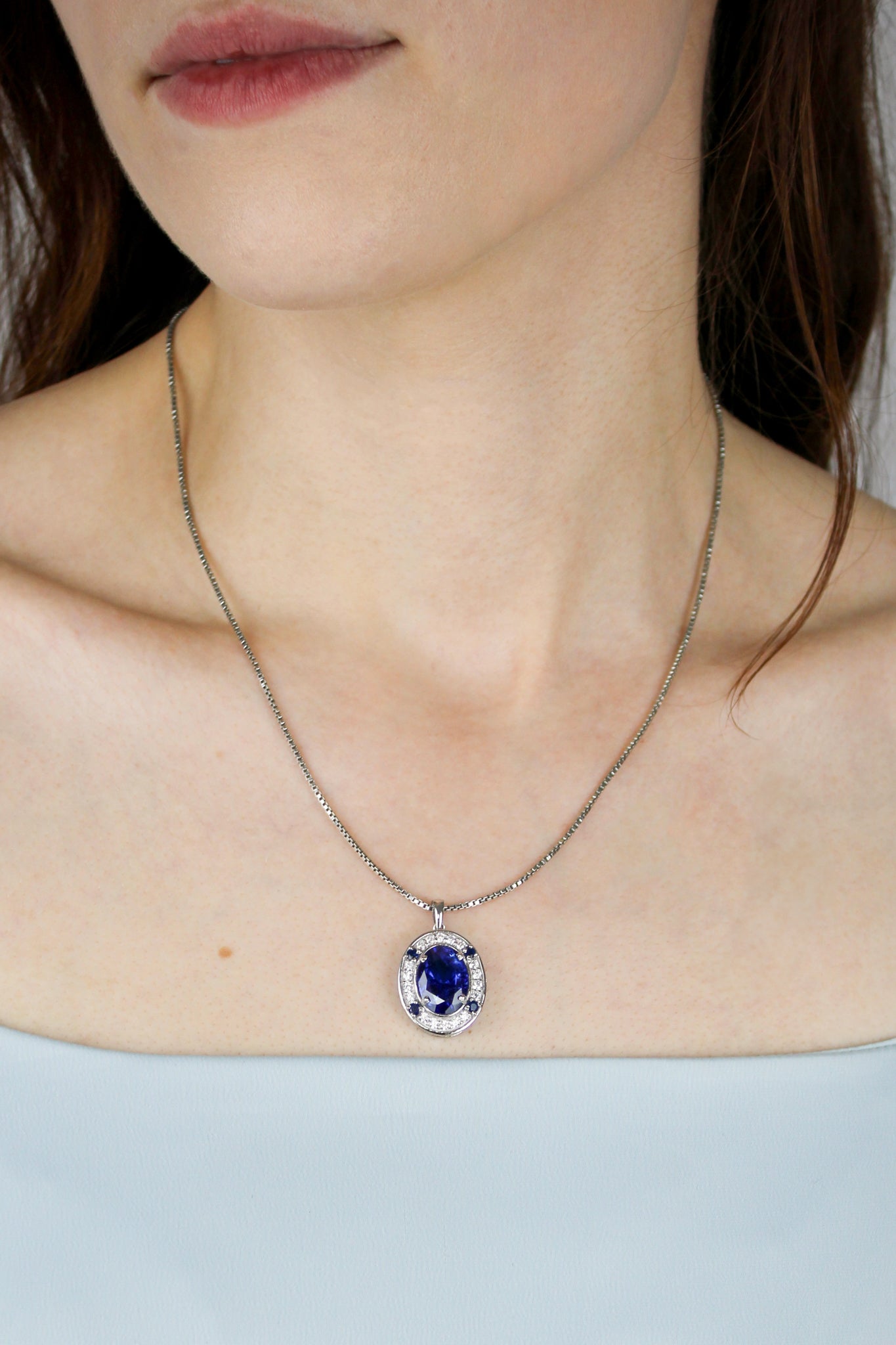 Close-up of silver Heartline Necklace resting on model’s collarbone, radiant blue gemstone catching light, Ether Jewelry