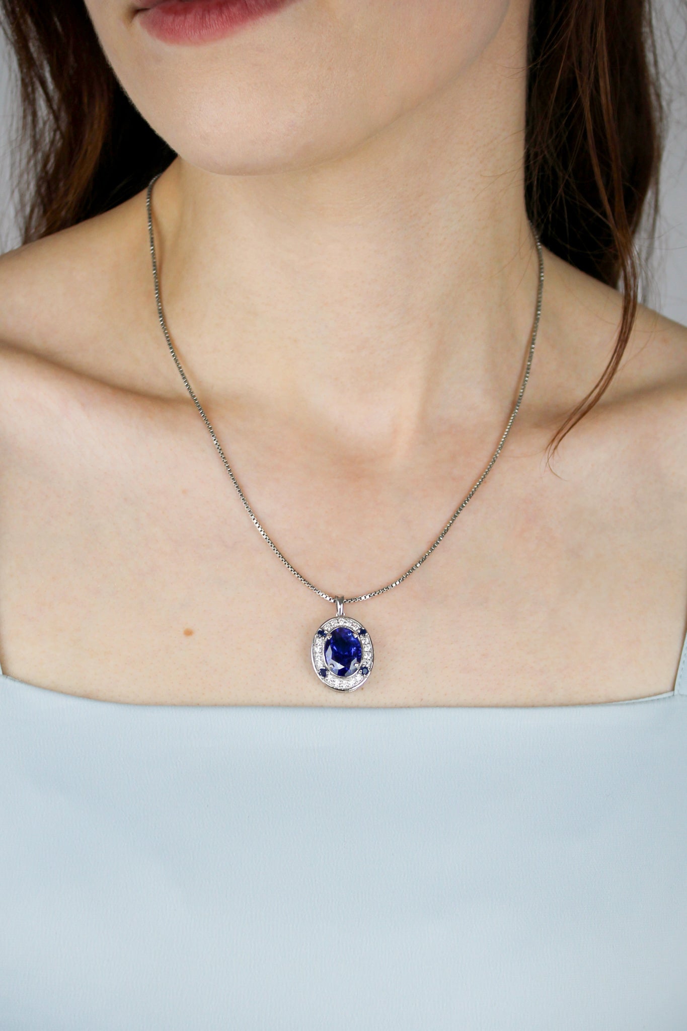 Close-up of silver Heartline Necklace resting on model’s collarbone, radiant blue gemstone catching light.