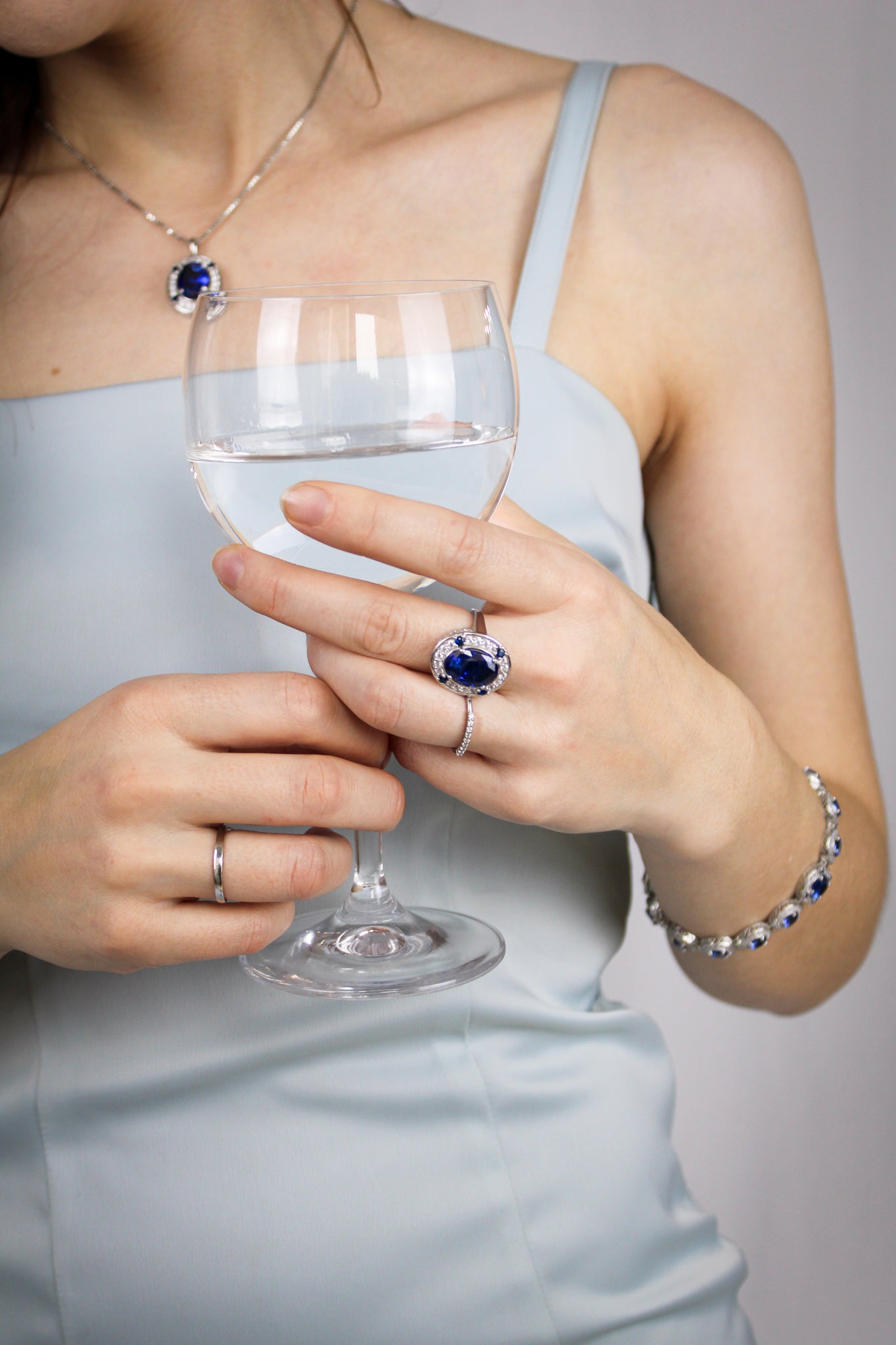 Close-up of silver Legacy Collection, Ring, Bracelet, Neckalce on model’s hand holding wine glass, reflecting refined craftsmanship and ethereal light.