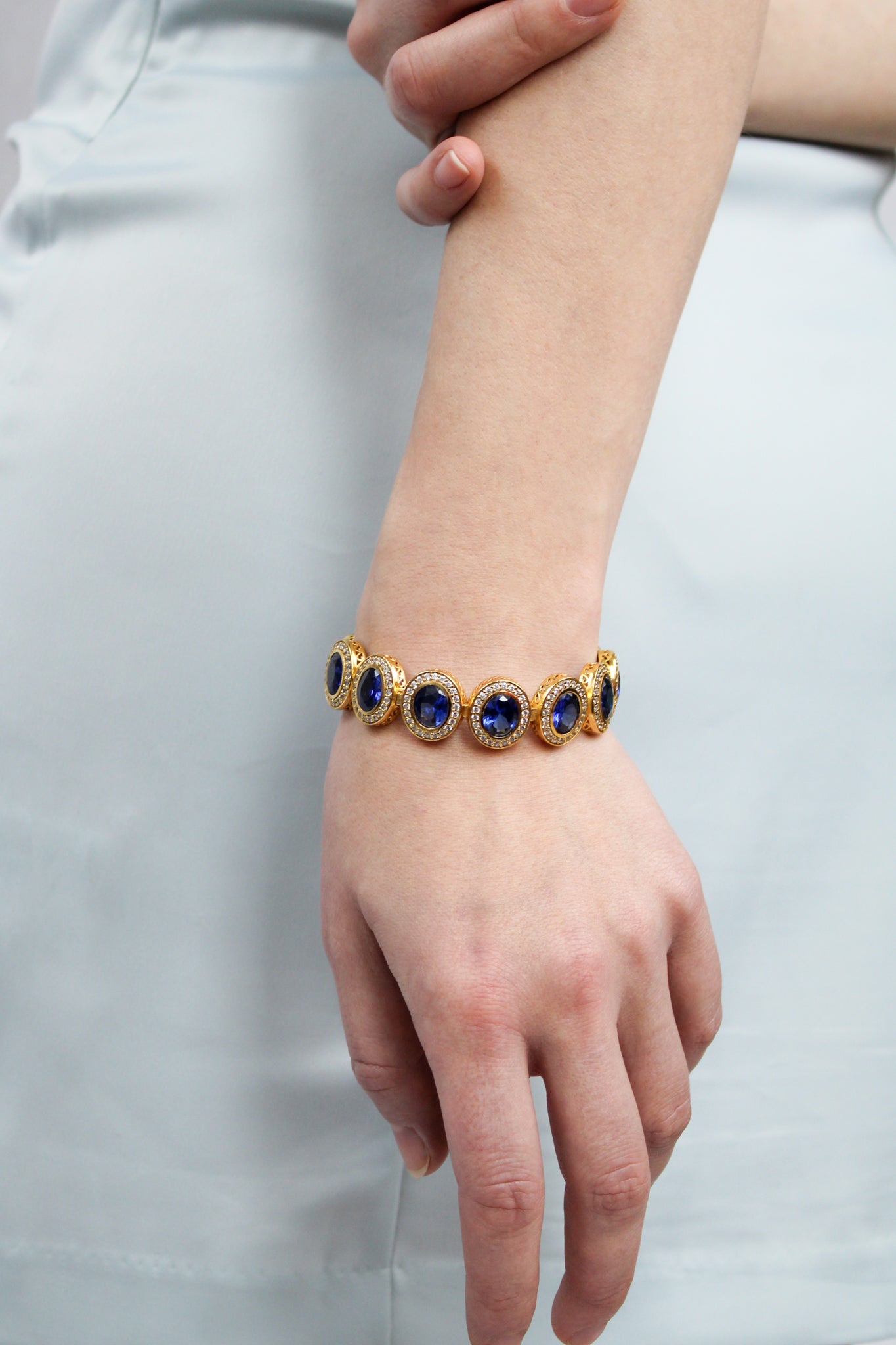 Model wearing gold Halo Bracelet adorned with sapphire and white gemstones — a tribute to Princess Diana’s light.