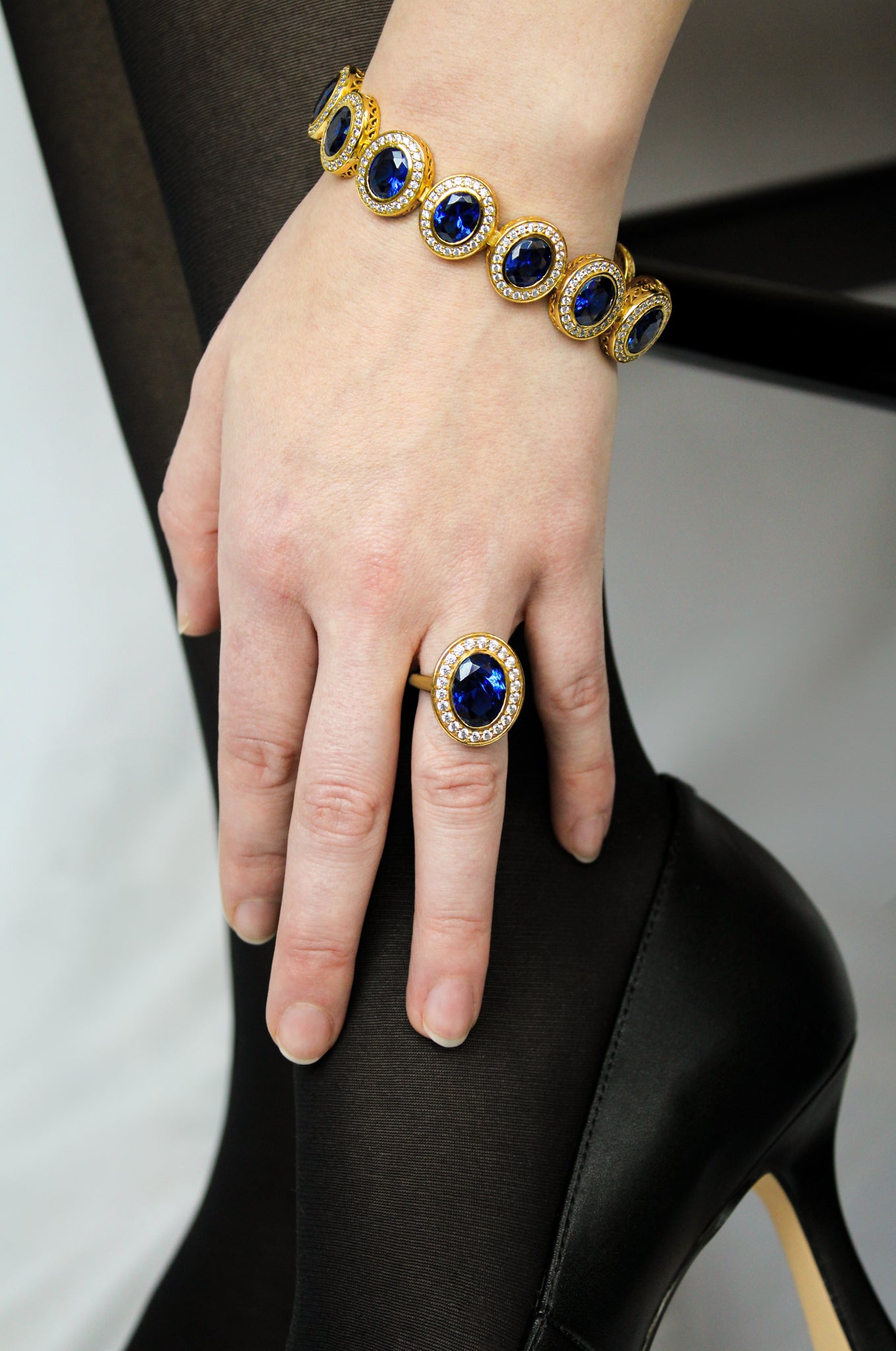 Gold Legacy bracelet and ring with blue gemstones on a hand against a neutral background