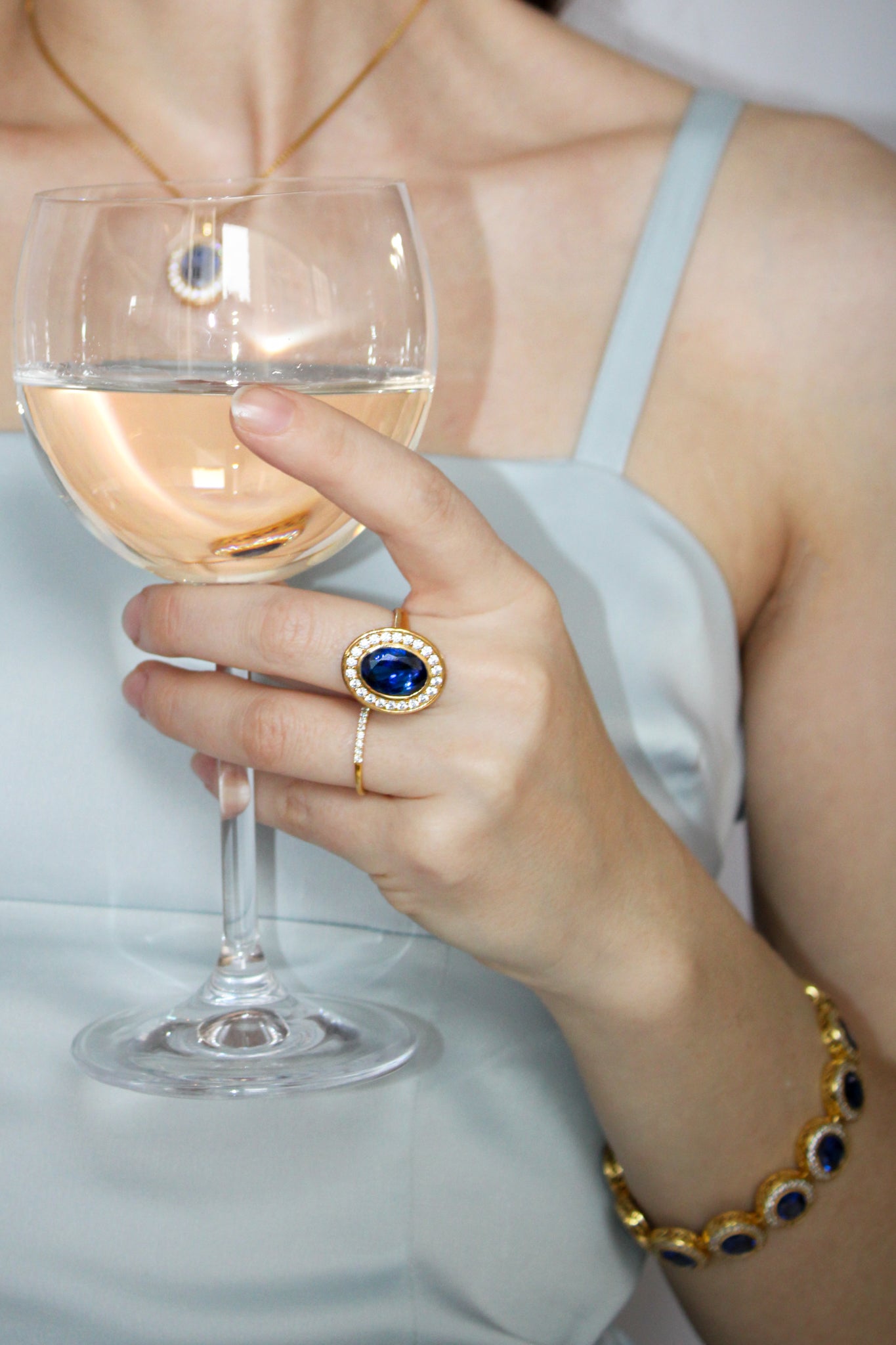 Model’s hand holding wine glass wearing gold Halo Bracelet — light catching sapphire halos beautifully.