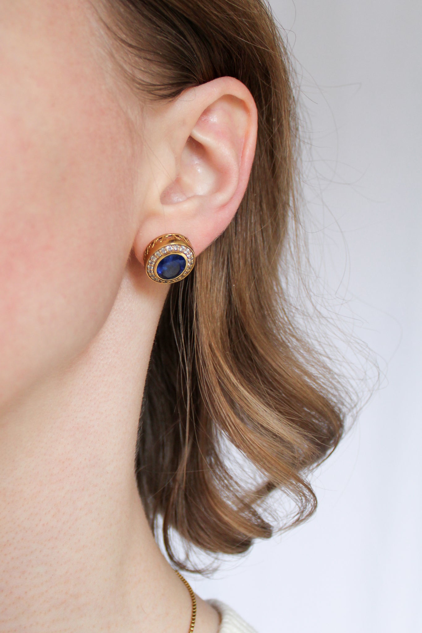Model wearing gold Sovereign Stud Earrings with sapphire-toned centers, inspired by Princess Diana’s regal charm.