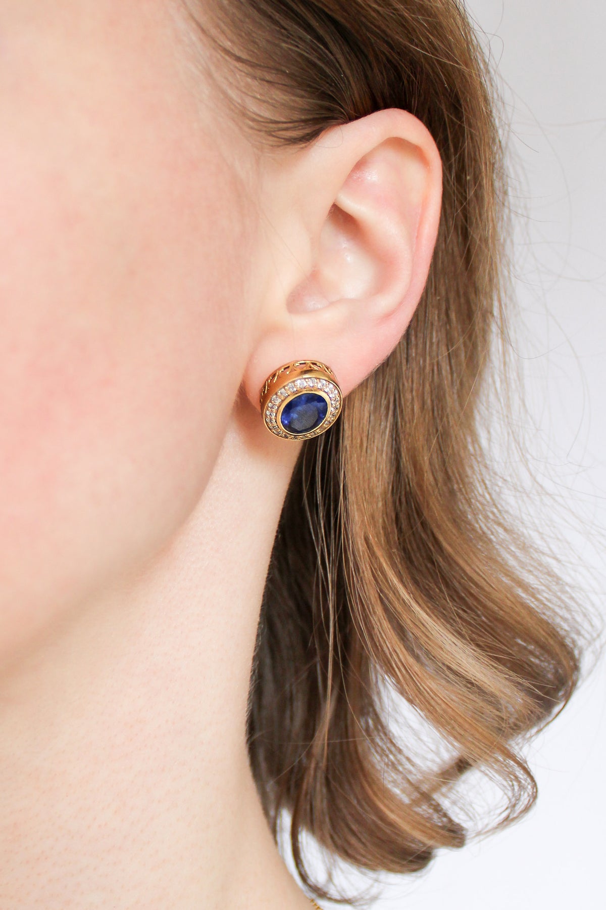 Model wearing gold Sovereign Stud Earrings with sapphire-toned centers, inspired by Princess Diana’s regal charm, Ether Jewelry