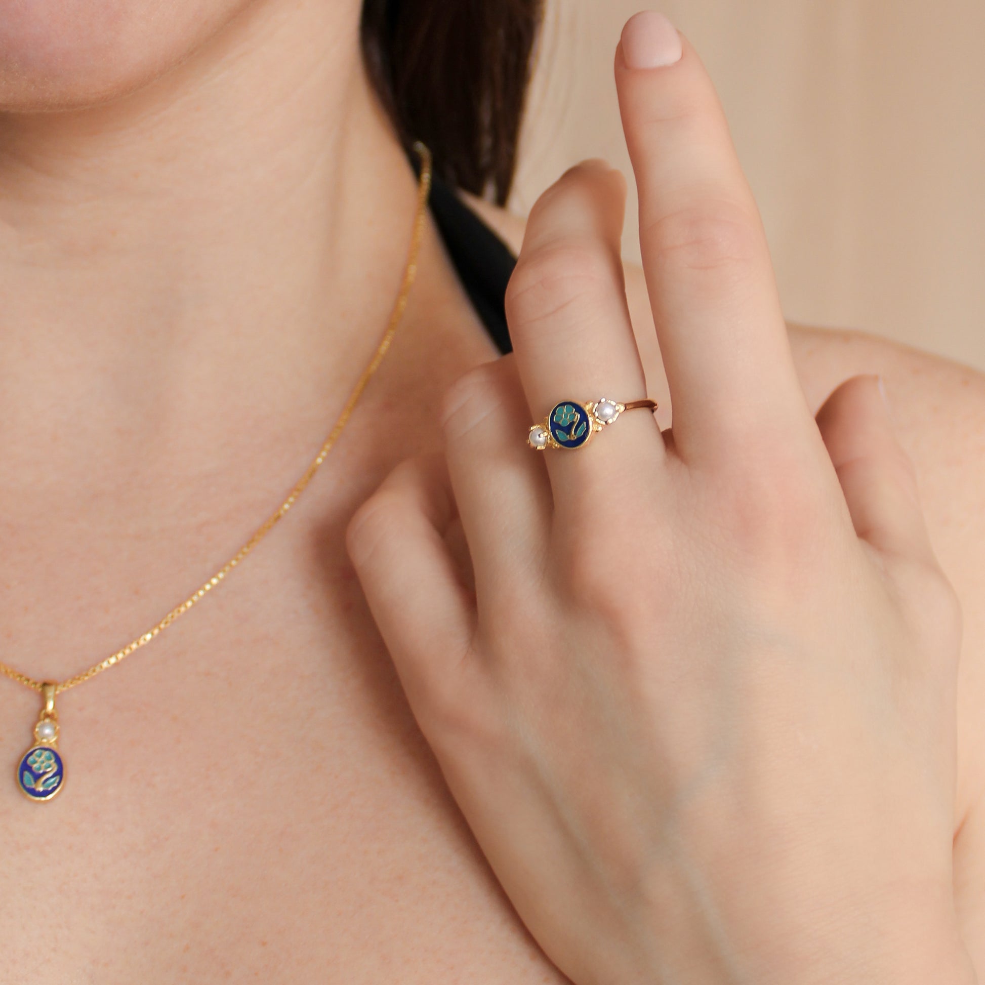 18k gold vermeil Mourning Bloom ring on hand held up next to necklace, blue enamel forget-me-not ring, Ether Jewelry