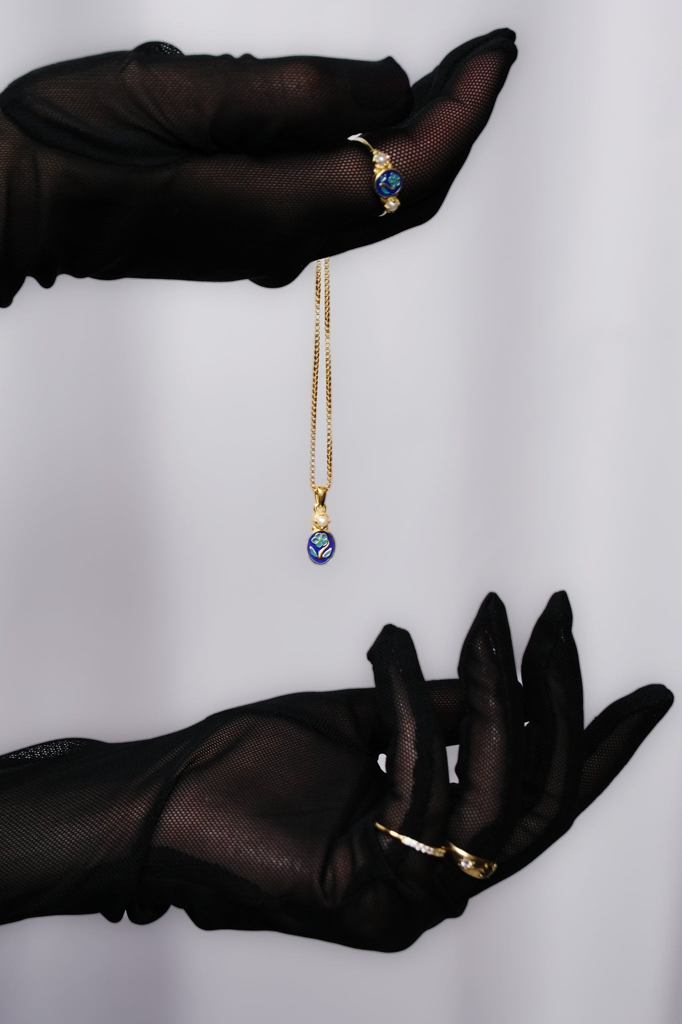 Black gloved hand dramatically holding Mourning Bloom 18k gold vermeil pendant, blue enamel forget-me-not necklace, Ether Jewelry