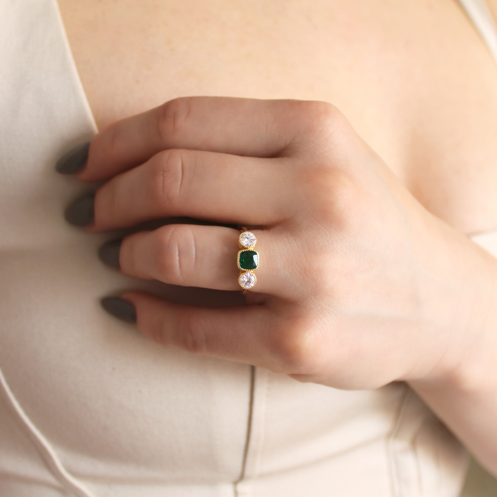 Edwardian Three Stone ring in 18k gold vermeil worn on model in beige dress, hand near chest, green CZ three stone ring, Ether Jewelry
