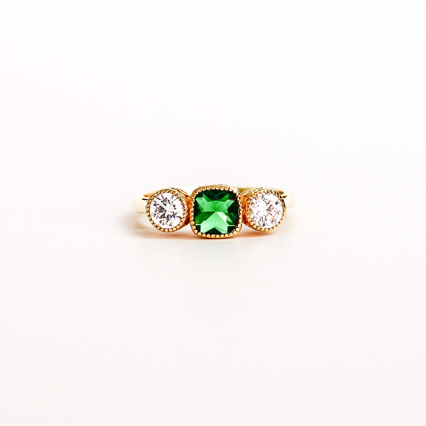 Three Stone Edwardian Ring on white background, square center emerald gemstone, two white side gemstones, ether jewelry