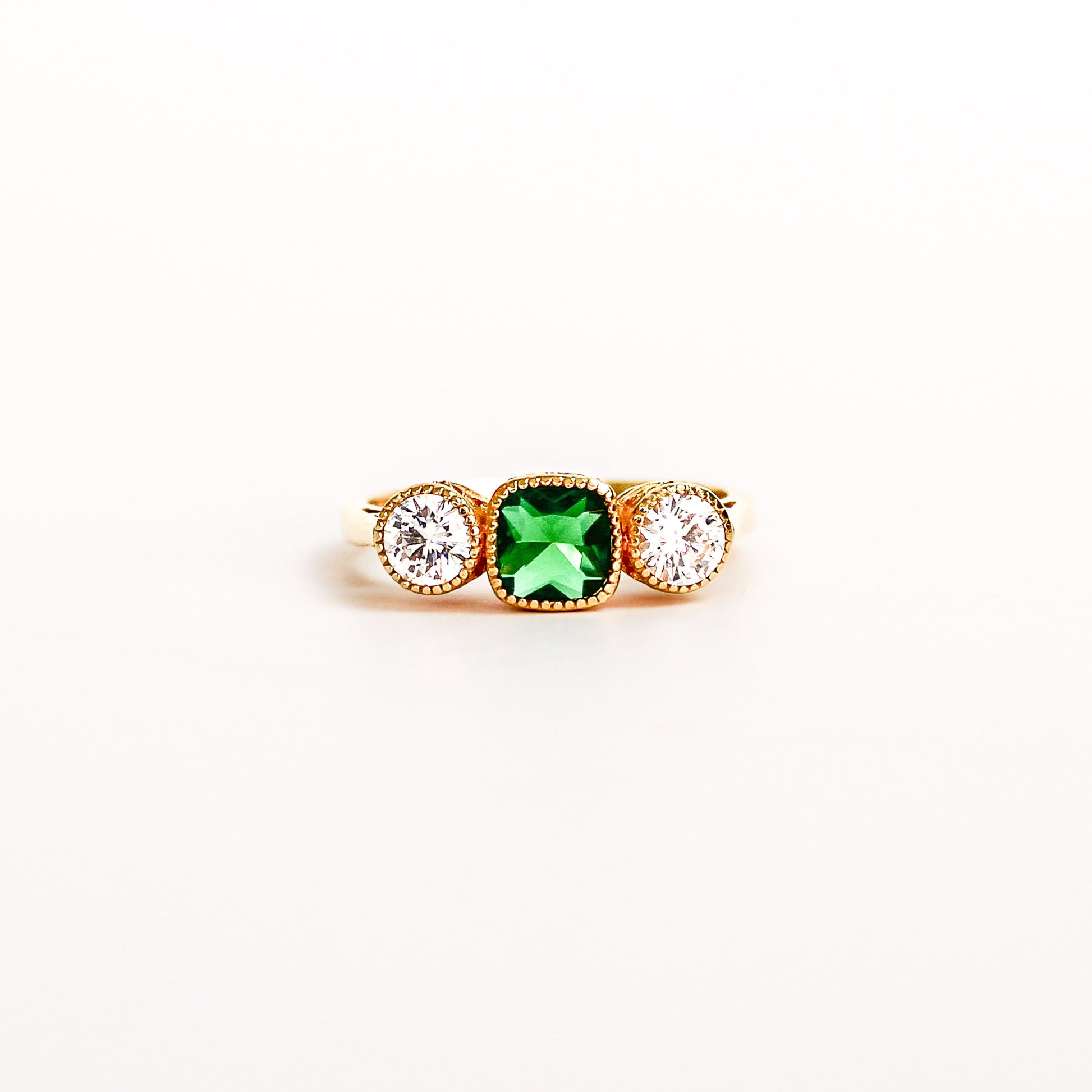 Three Stone Edwardian Ring on white background, square center emerald gemstone, two white side gemstones, ether jewelry