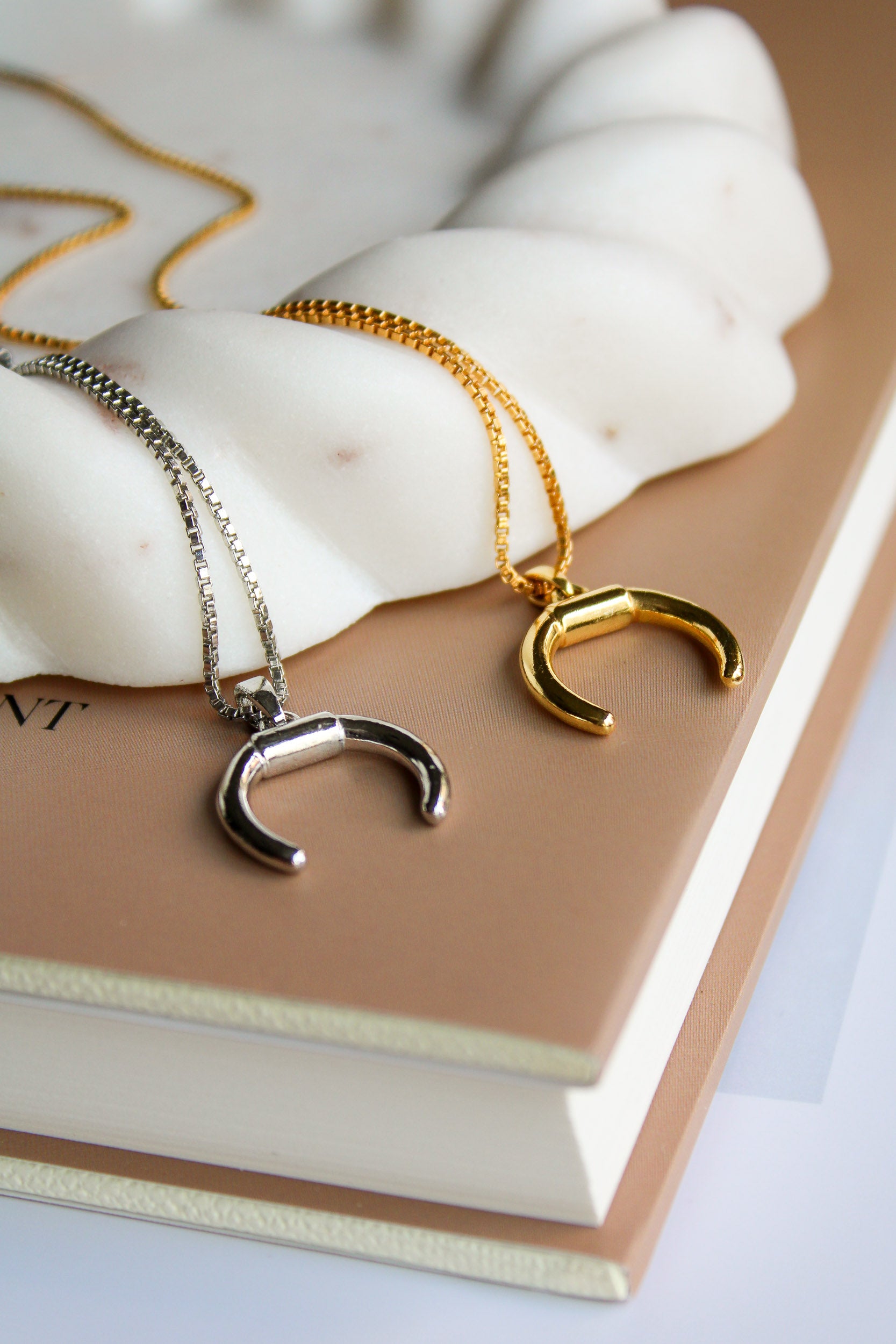 18k gold vermeil Ether Necklace staged on book, double horn pendant flat lay, Ether Jewelry