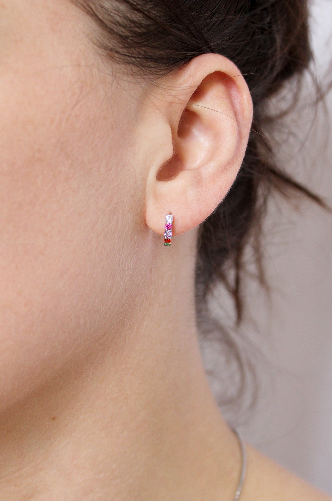 Sterling silver Regard Huggies close-up on model ear, colorful acrostic REGARD CZ stones on huggie hoop, Ether Jewelry