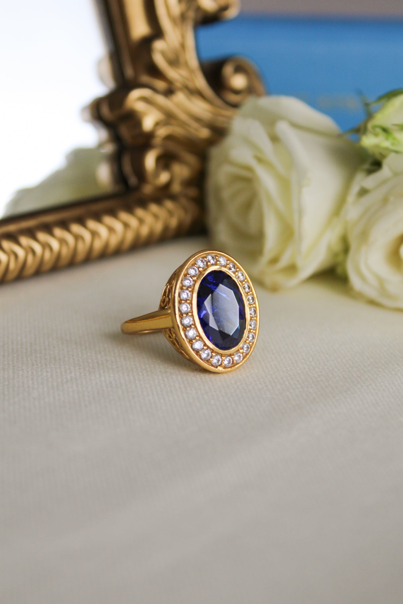 Gold Diana Legacy Ring featuring sapphire-blue center stone surrounded by brilliant white accents on engraved band.