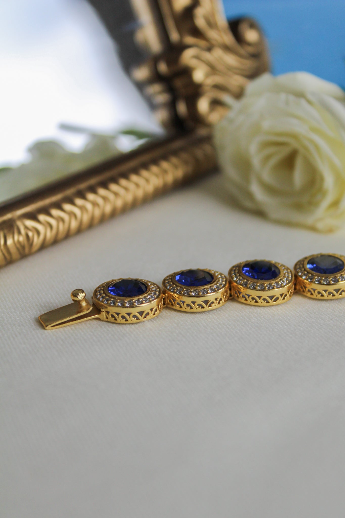 Close-up of gold Halo Bracelet featuring blue sapphire and white stone halos on engraved gallery links.