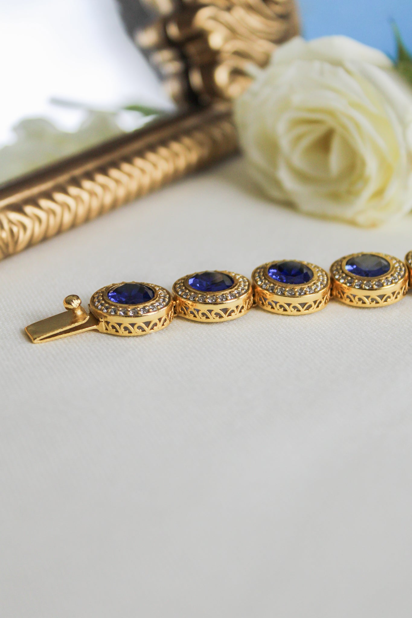 Close-up of gold Halo Bracelet featuring blue sapphire and white stone halos on engraved gallery links, Ether Jewelry