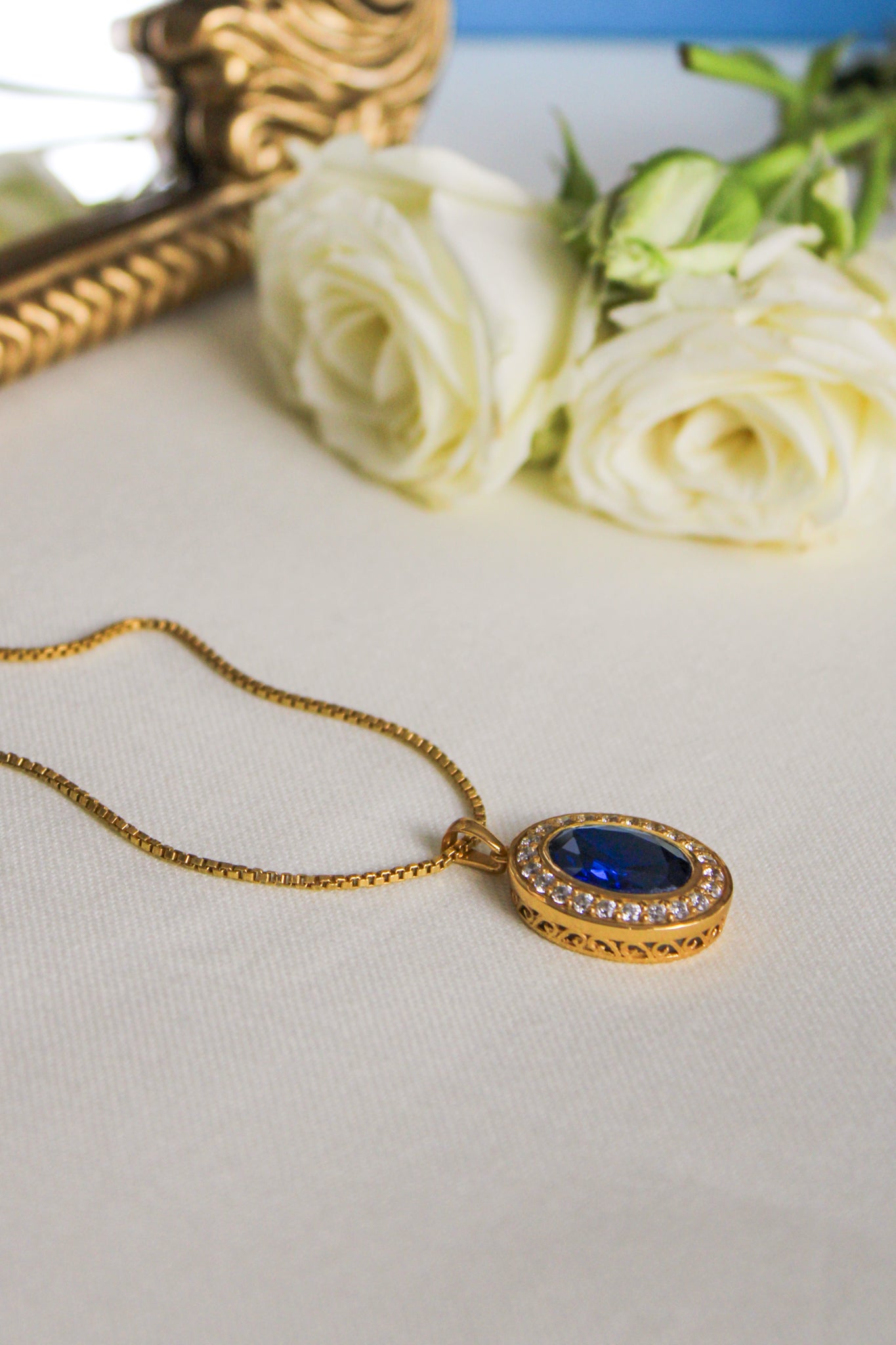 Close-up of gold Heartline Necklace featuring radiant blue center stone on box chain.