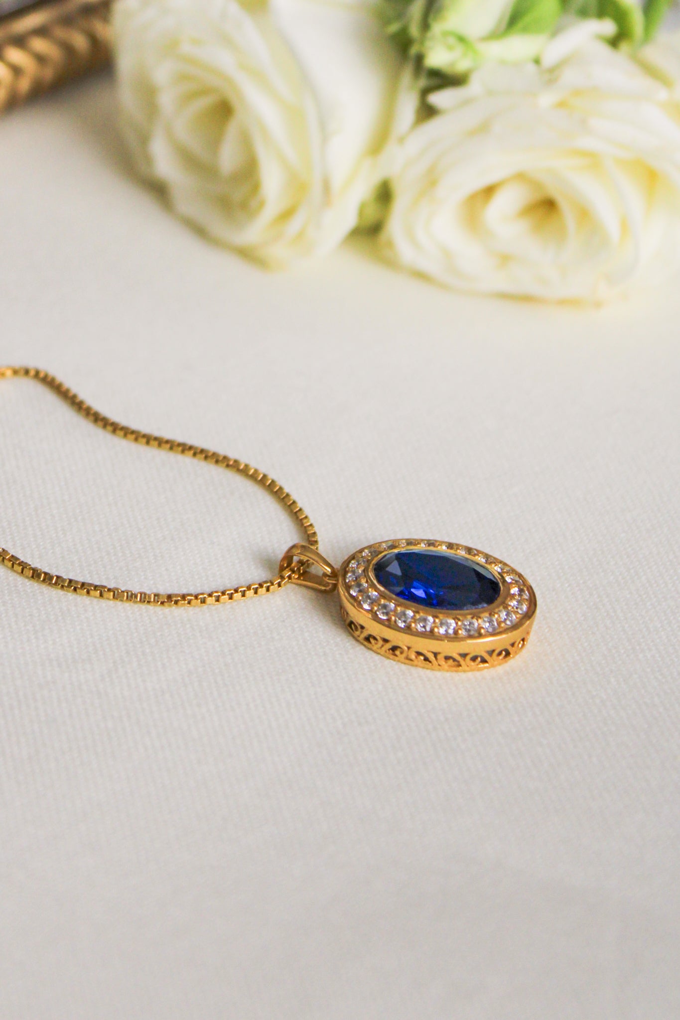 Close-up of gold Heartline Necklace featuring radiant blue center stone on box chain, Ether Jewelry