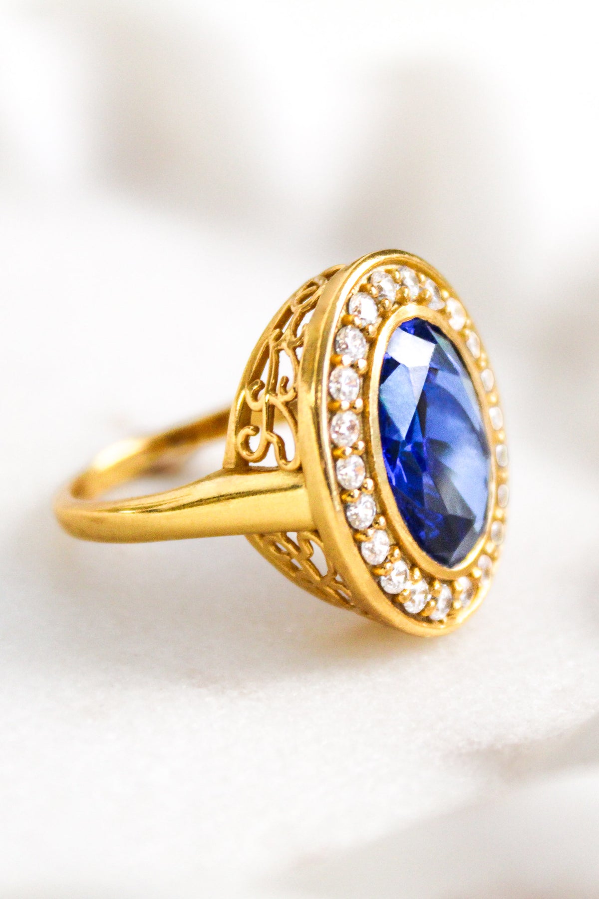 Marco shot of Gold ring with a blue gemstone and diamond accents on a white background, Ether Jewelry
