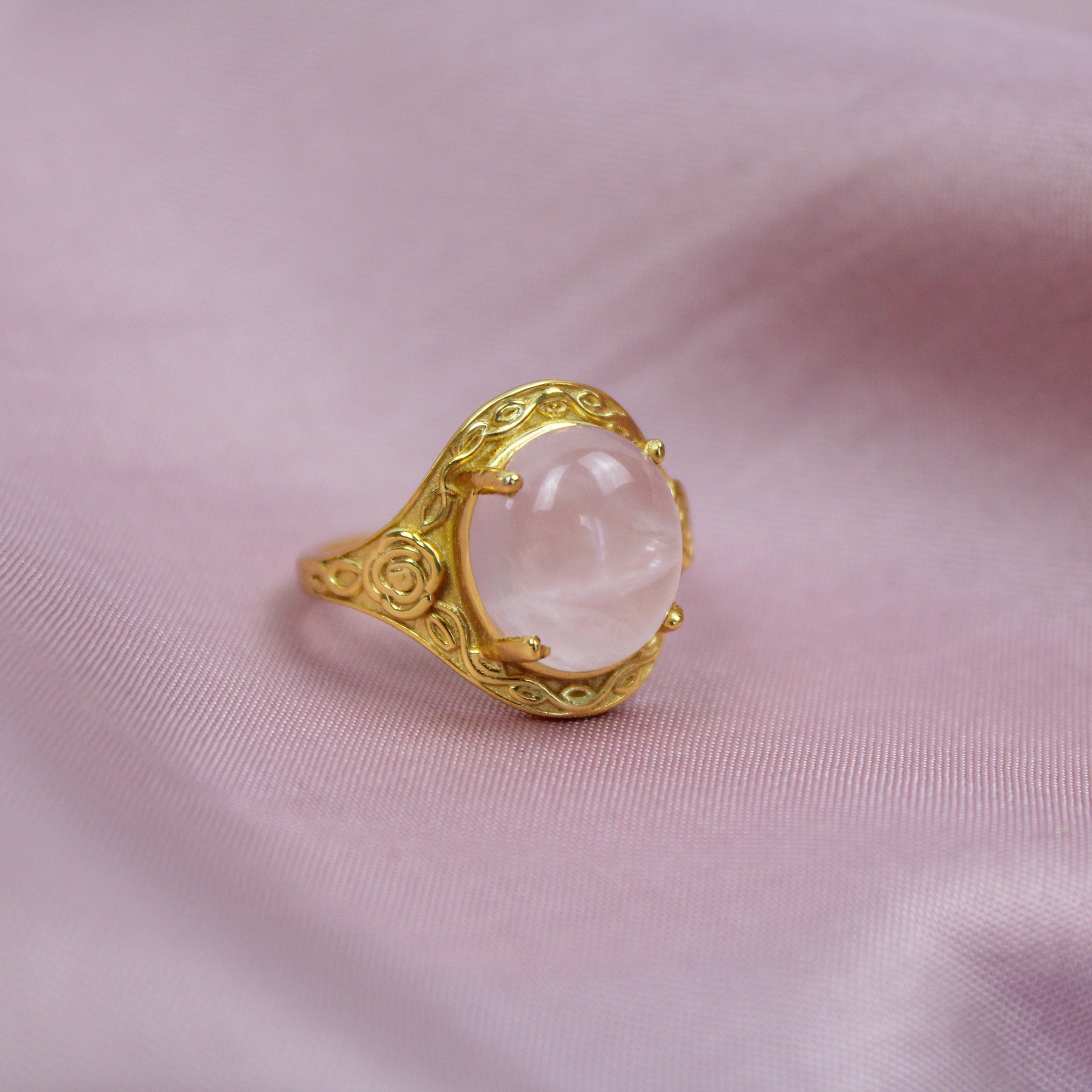 Gold romantic heir signet ring with a pink quartz stone and flower engravings on a pink fabric background
