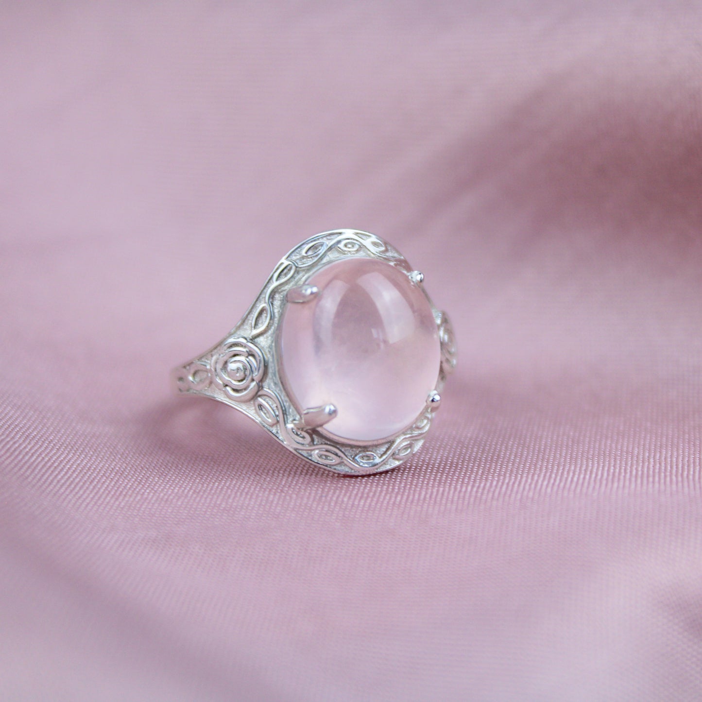 Silver romantic heir signet ring with a large pink quartz stone and flower engravings on a pink fabric background