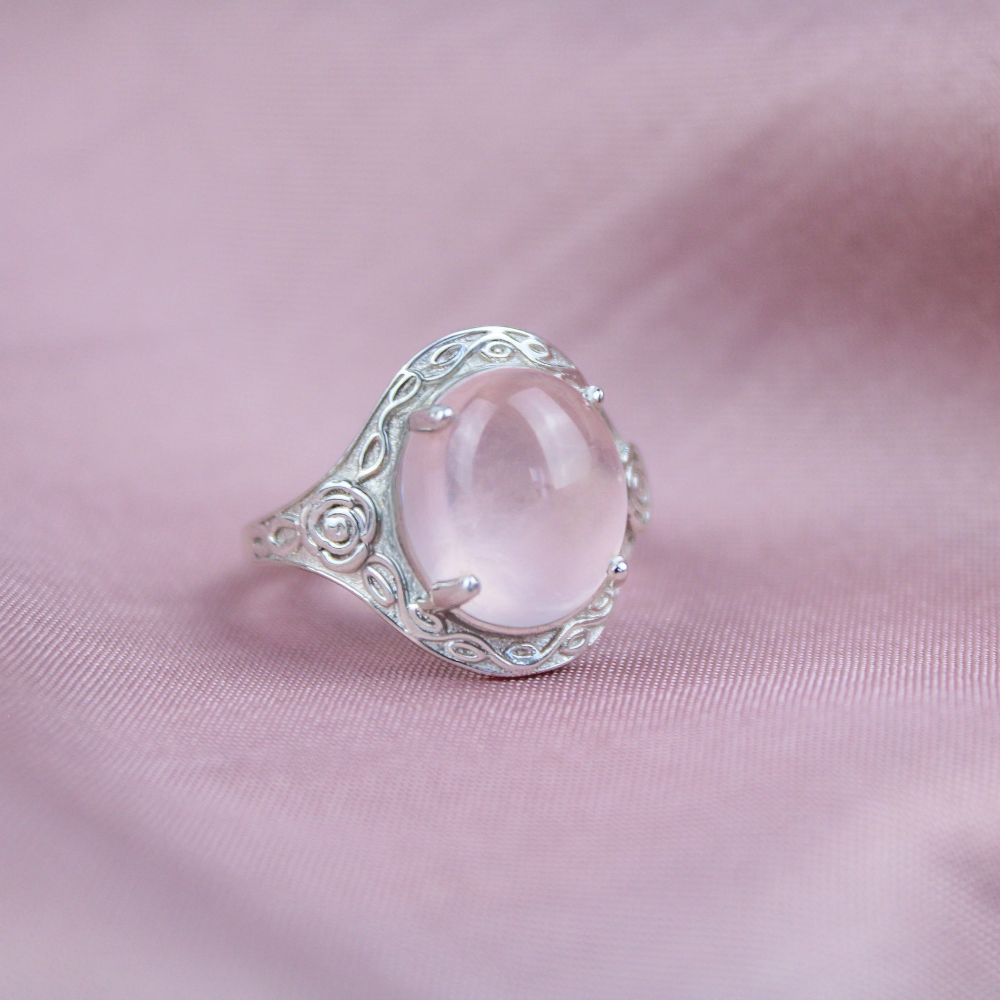 Silver romantic heir signet ring with a large pink quartz stone and flower engravings on a pink fabric background