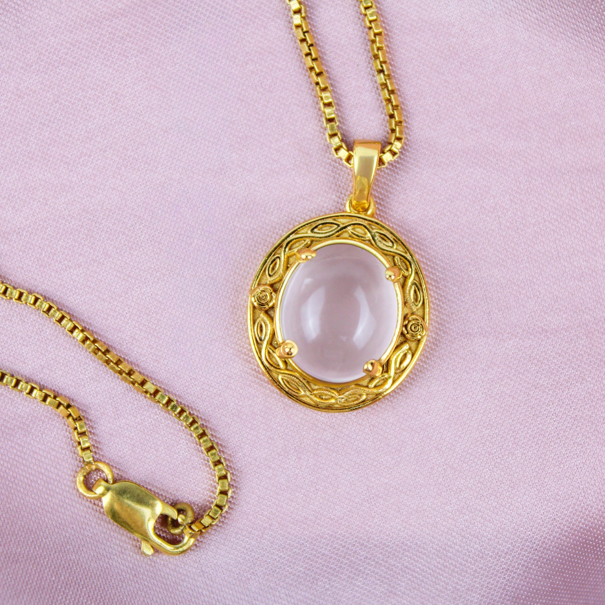 Gold Romantic Heir necklace with a round pendant and flower engravings on a pink background