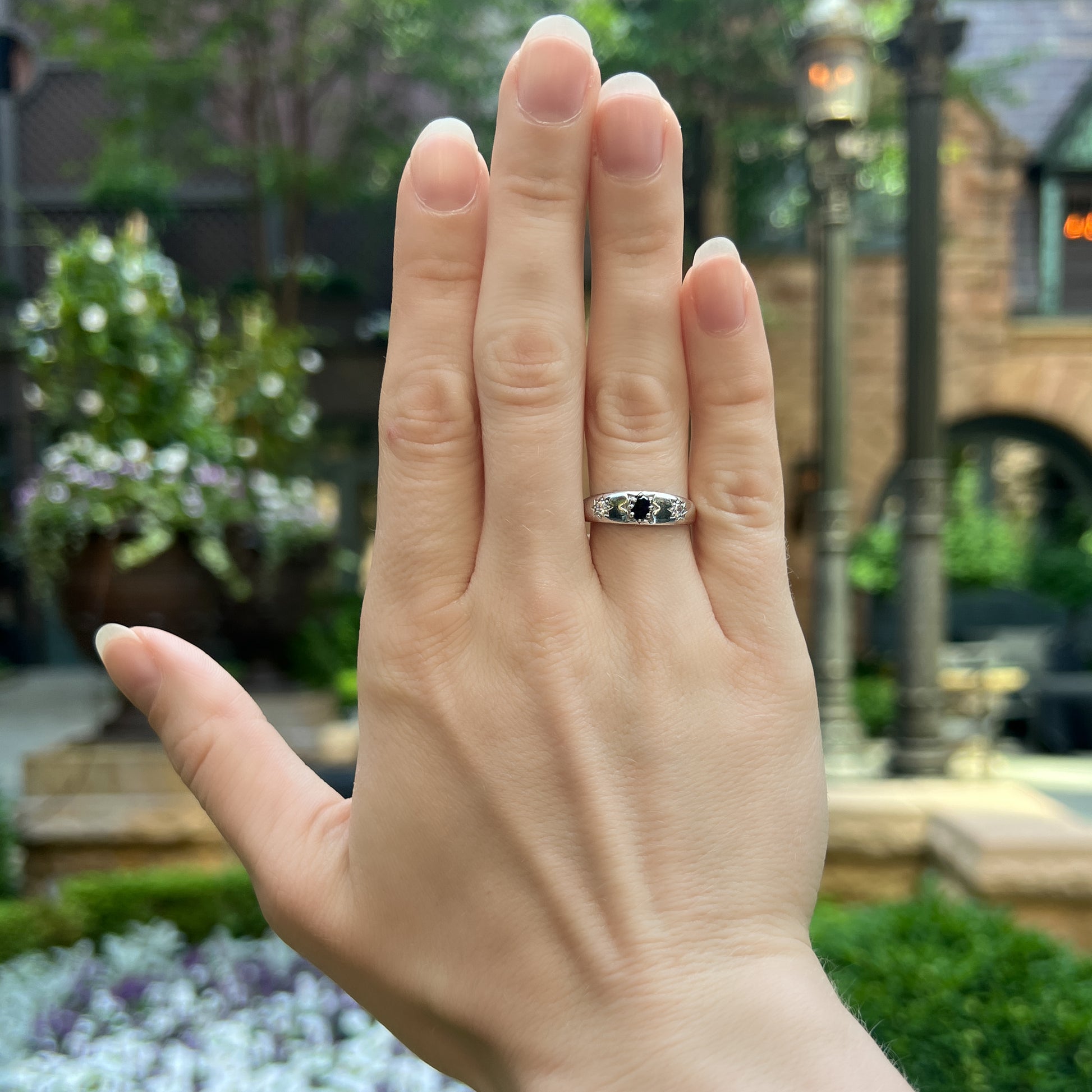 Midnight Roma sterling silver ring worn on hand in front of flowers, three star-set CZ domed band, Ether Jewelry