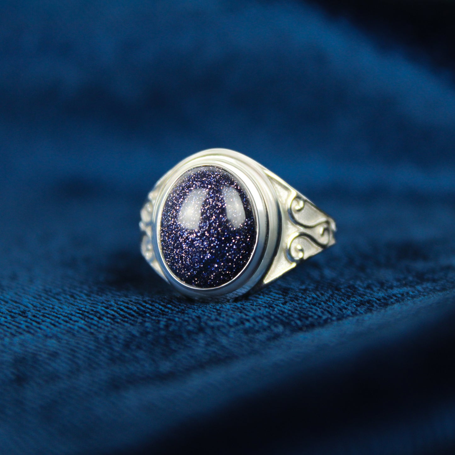 Silver night keeper signet ring with a blue sandstone gemstone on a blue fabric background