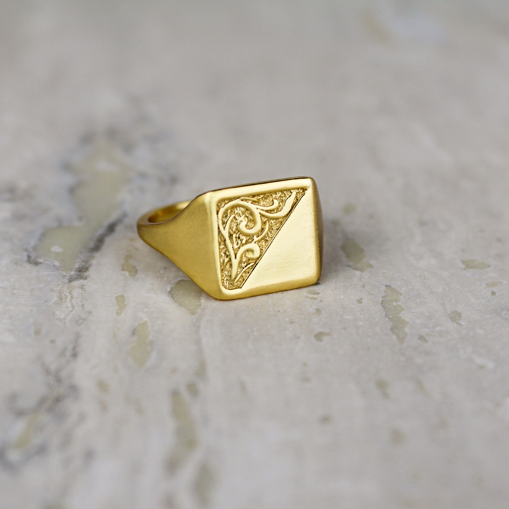 Gold square architect signet ring with intricate design on a marble surface